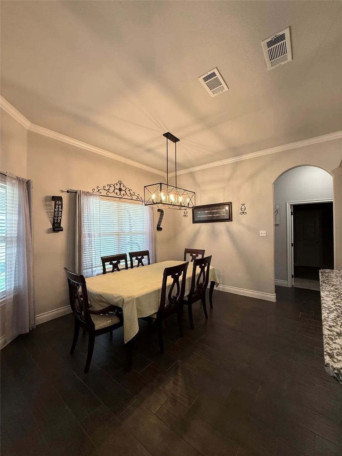 Dark wood-finish flooring, crown molding, and a modern rectangular chandelier illuminate the dining space