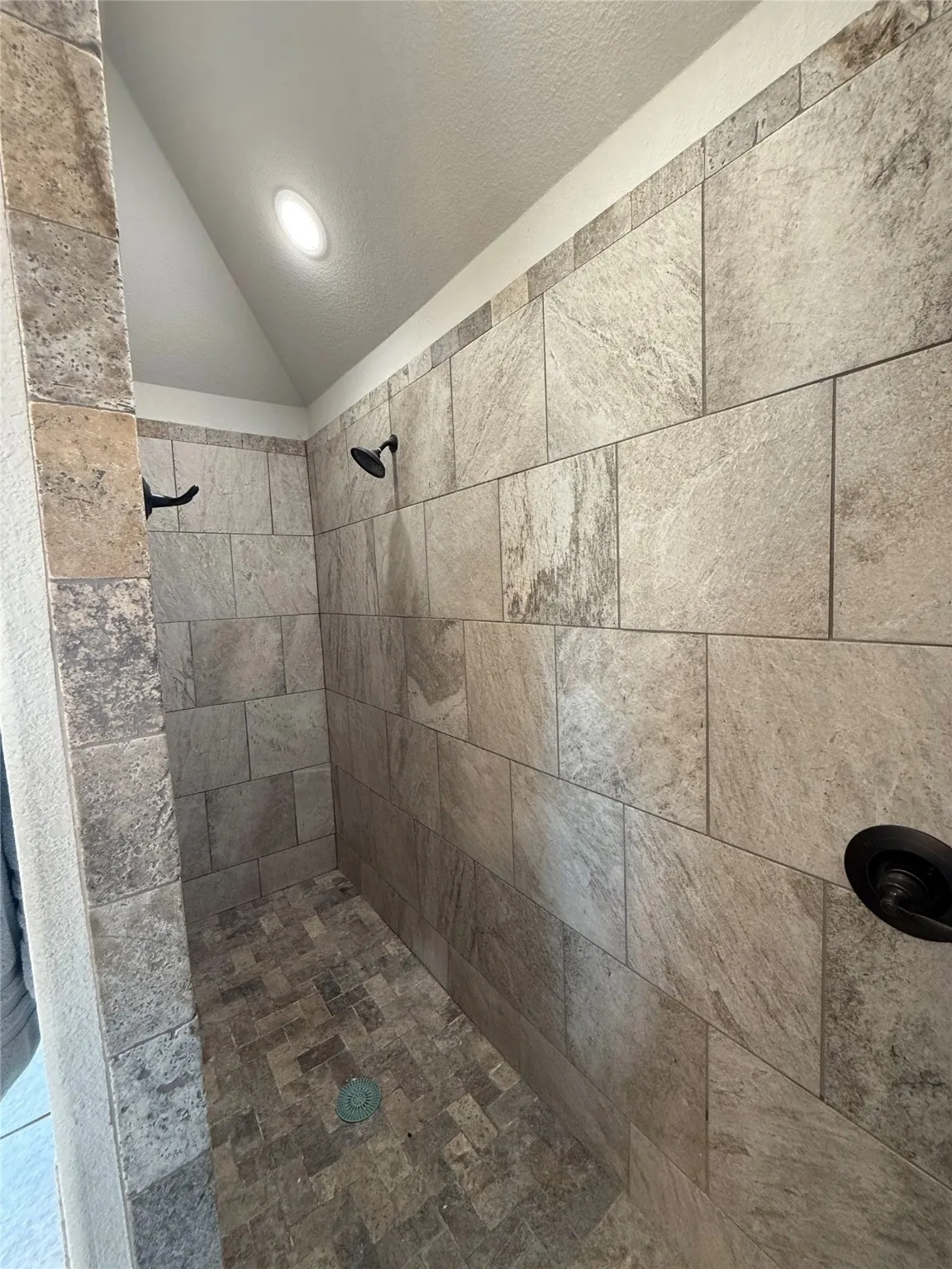 Tiled shower with a sloped ceiling and recessed lighting, featuring a contrasting floor tile pattern and matte black fixtures