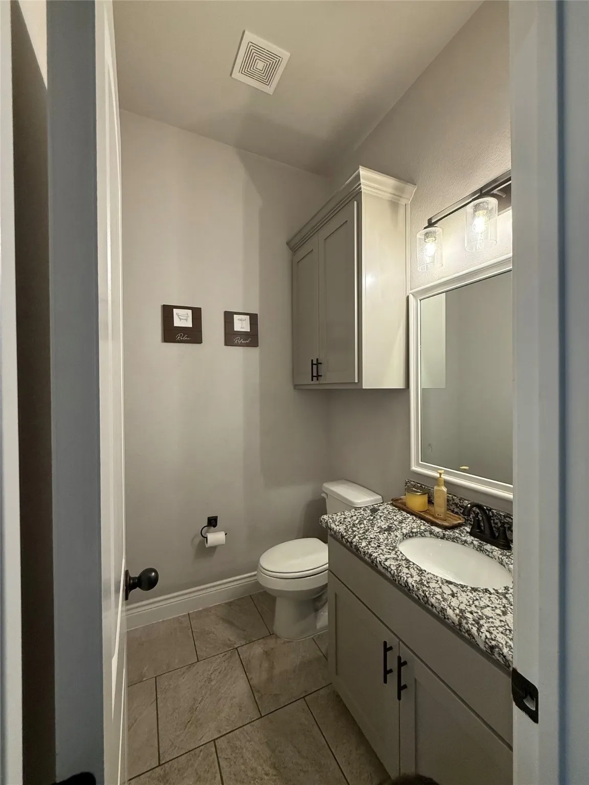 Light gray vanity with black hardware, white rectangular sink, and stone-finish countertop