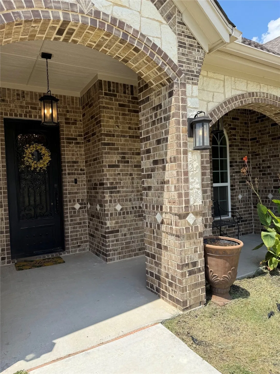 Brick and stone exterior with arched entryways, concrete porch, and decorative wall sconce