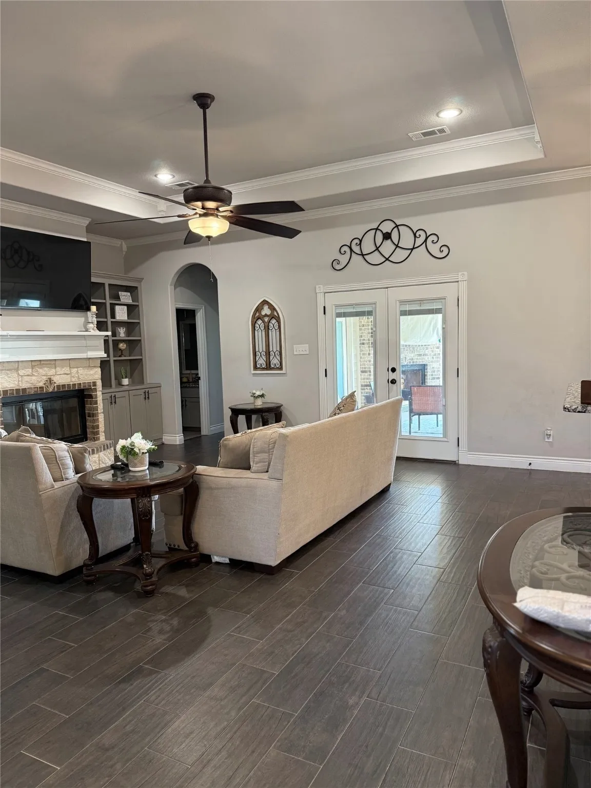 Recessed lighting and ceiling fan, tray ceiling with crown molding, built-in shelving, stone fireplace surround, and wood-look tile flooring