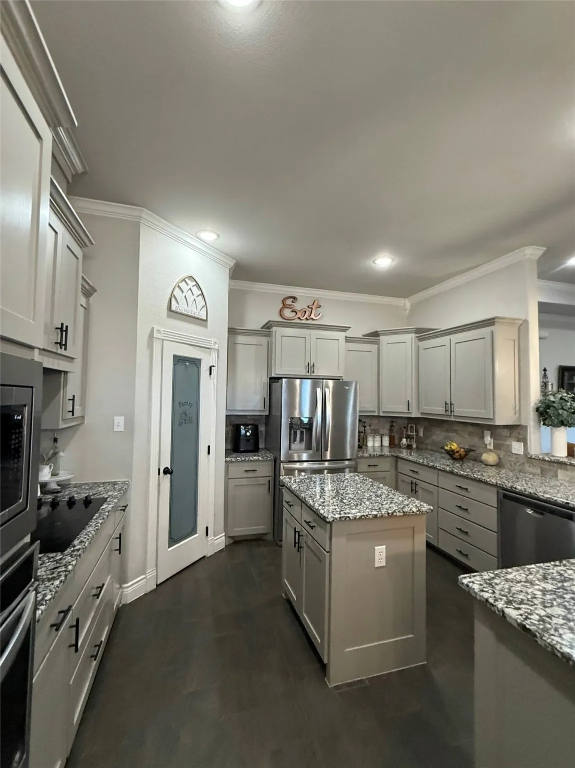 Kitchen featuring a central island, stainless steel appliances, light-toned cabinetry, and dark-finish flooring