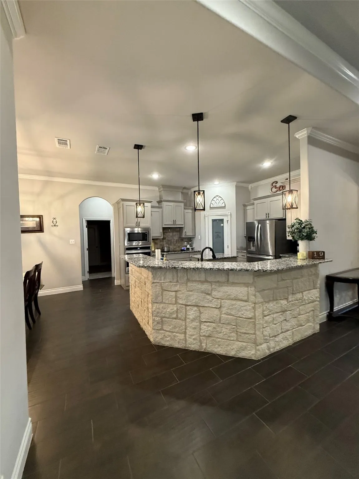 Kitchen featuring a stone-clad island, granite countertops, pendant lighting, stainless steel appliances, and dark tile flooring