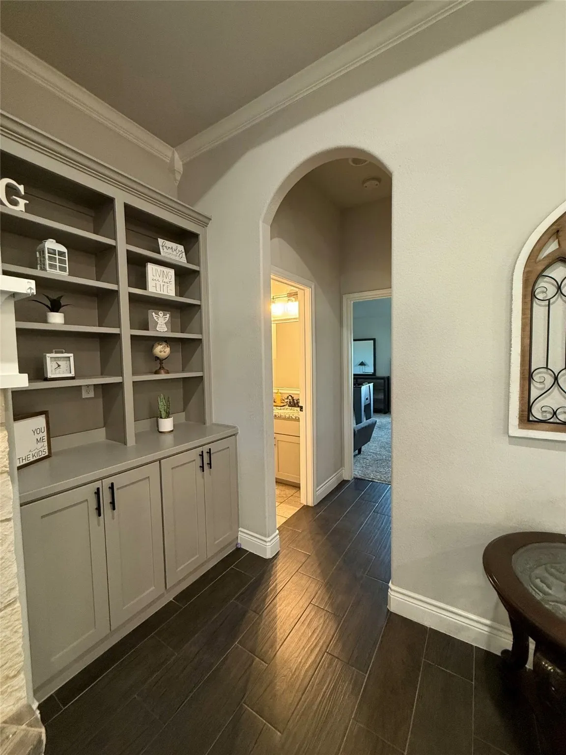 Built-in cabinetry with open shelving, arched hallway entry, and wood-finish flooring