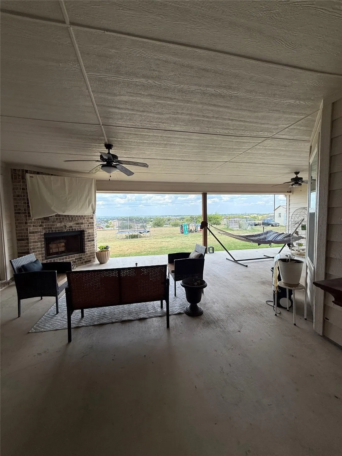 Expansive covered patio featuring a brick fireplace, concrete flooring, and ceiling fans