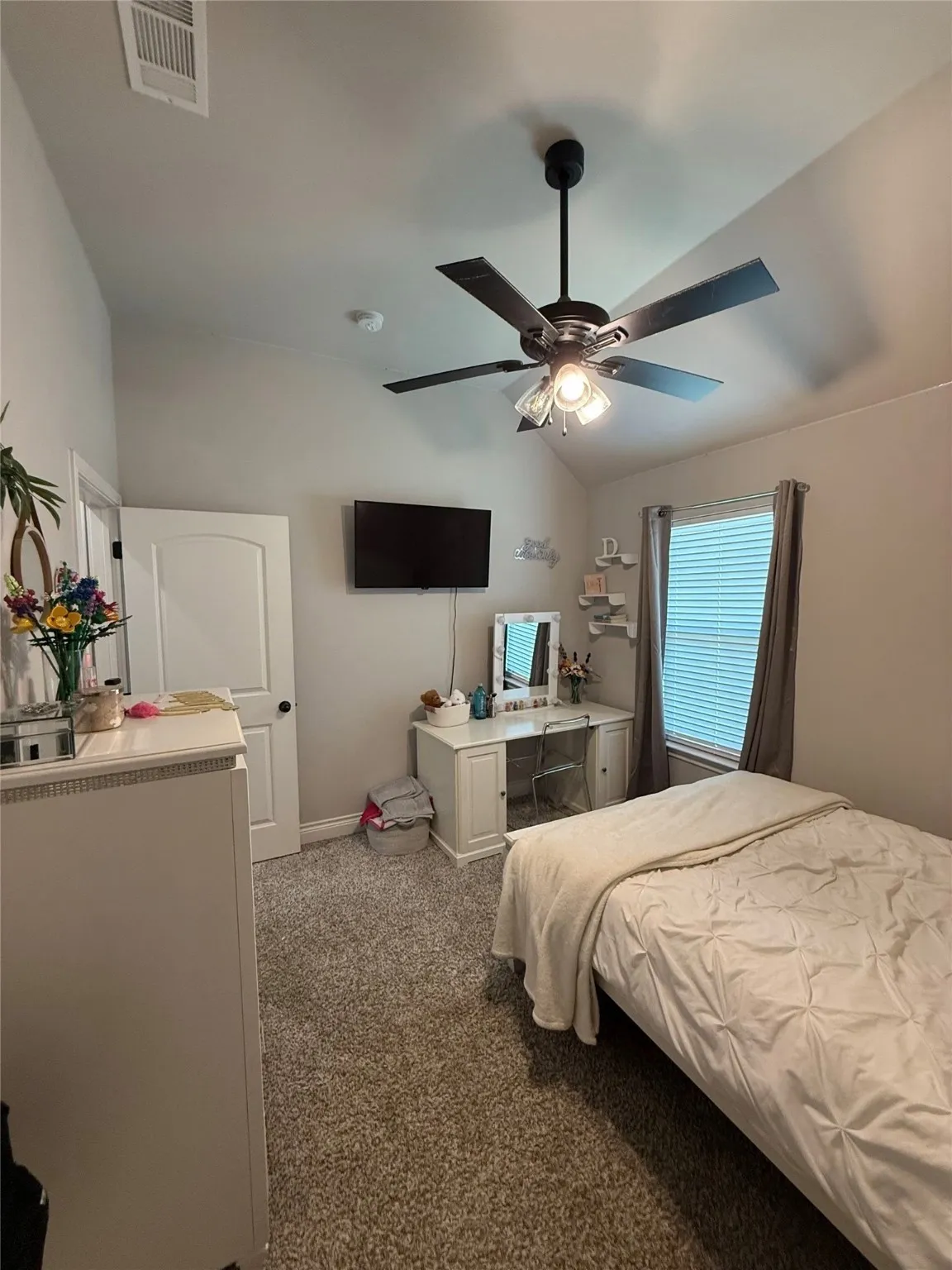 Vaulted ceiling with a ceiling fan light fixture, wall-mounted television, and textile window treatments