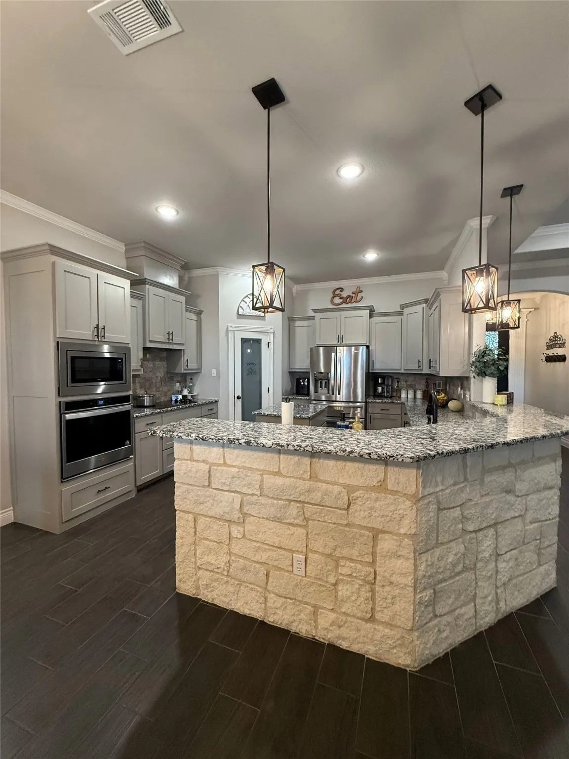 Kitchen featuring a stone-clad island with a composite countertop, wood-finish flooring, recessed lighting, and pendant light fixtures