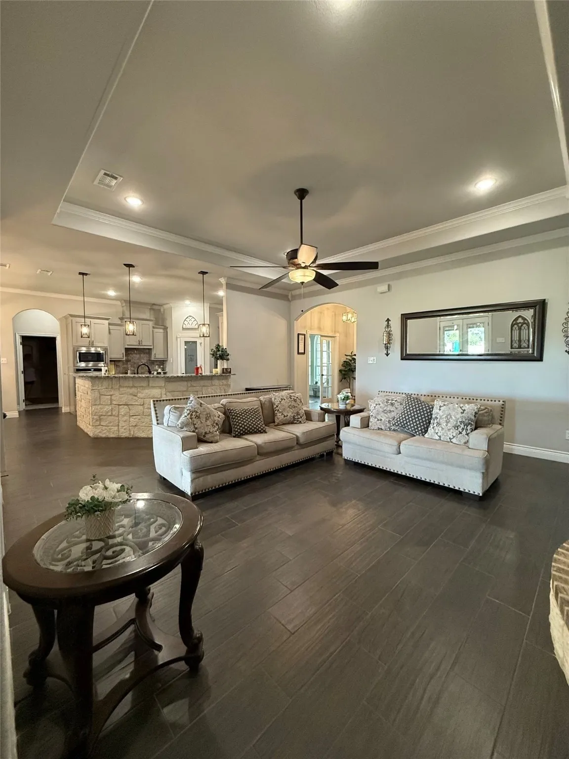 Spacious living area featuring wood-finish tile flooring, recessed lighting, and a tray ceiling with a ceiling fan