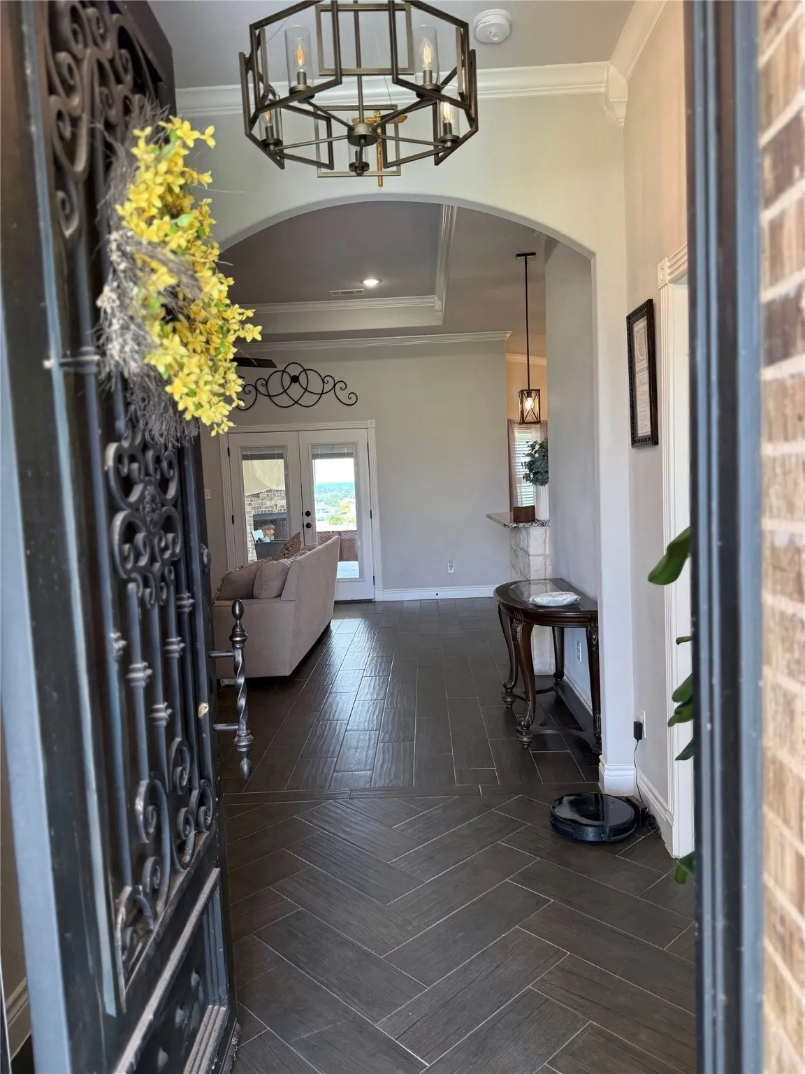 Entryway featuring a decorative wrought iron door, herringbone-patterned tile flooring, an arched doorway, and a tray ceiling with a dark bronze chandelier