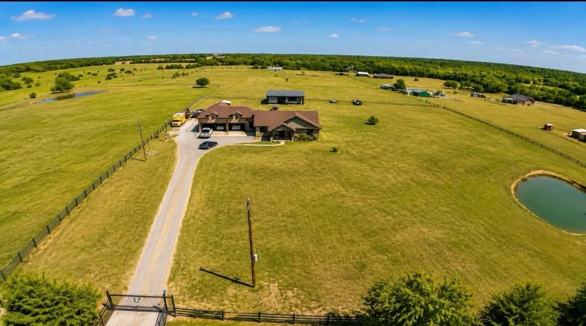 Expansive property featuring a main residence, secondary structure, private pond, and perimeter fencing, all surrounded by open green fields