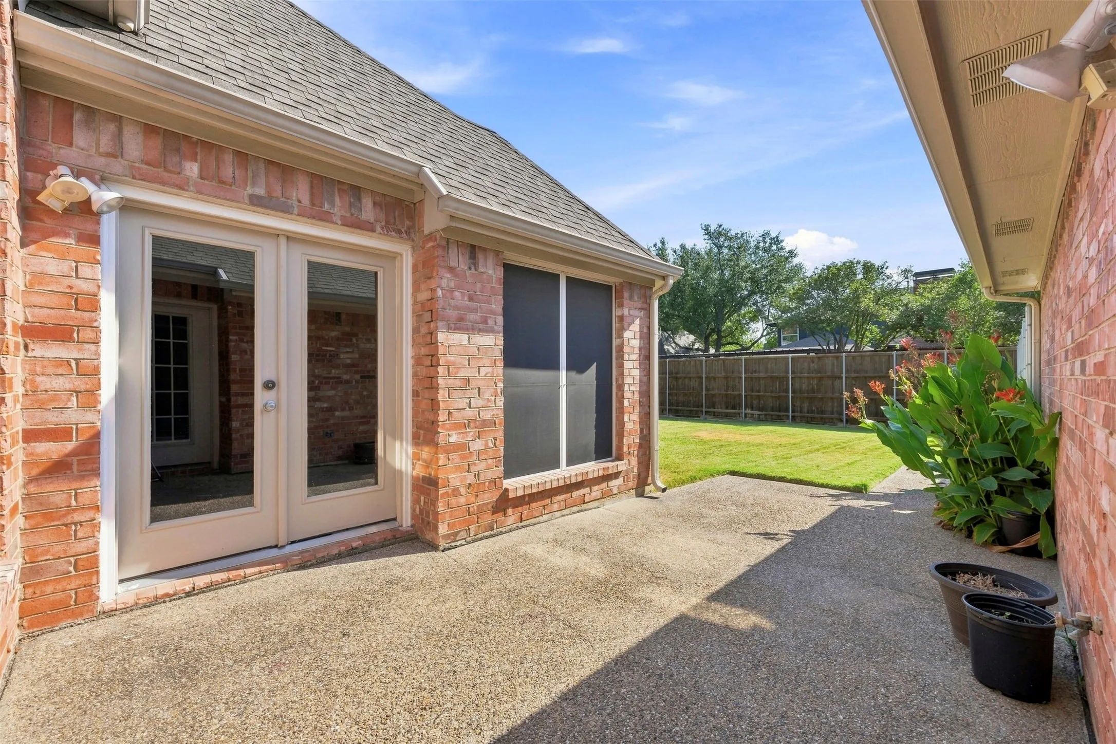 Brick exterior featuring a concrete patio, double glass-paneled doors, and a fenced backyard with a manicured lawn
