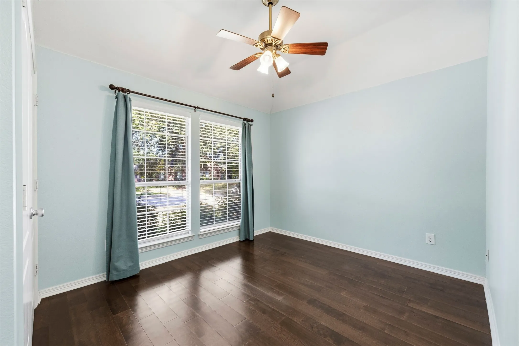 Wood-finish flooring, dual windows with blinds, ceiling fan with integrated lighting, and light blue wall finish