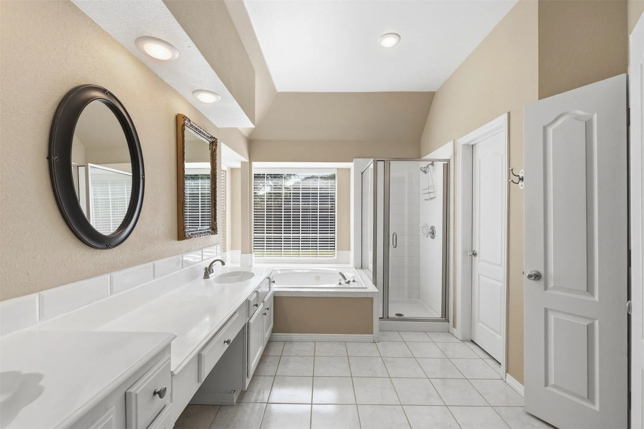 Dual vanity with integrated sinks, built-in soaking tub, glass-enclosed shower, tiled flooring, and recessed lighting