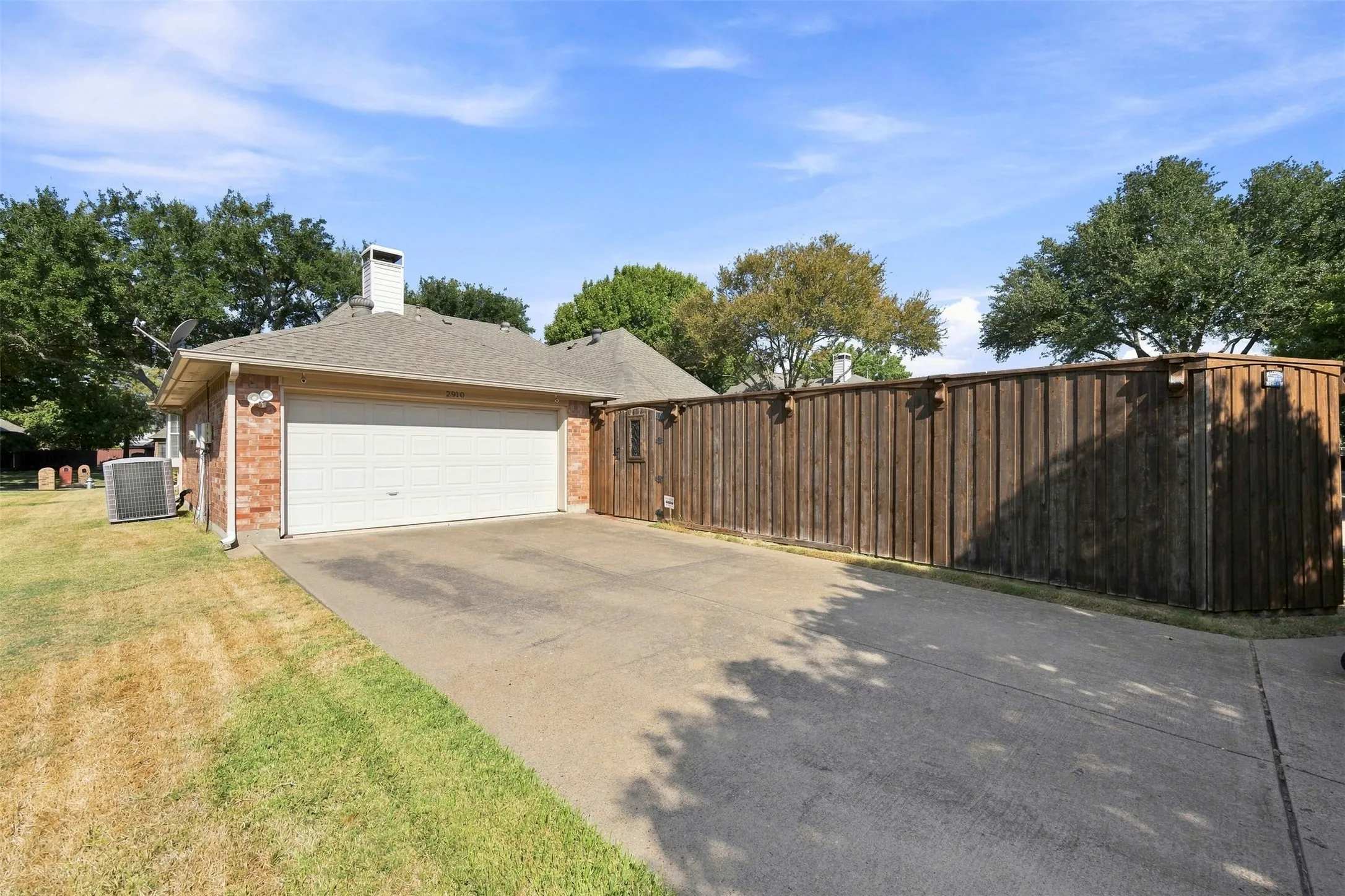 Attached two-car garage with a concrete driveway, brick exterior, and a wood privacy fence