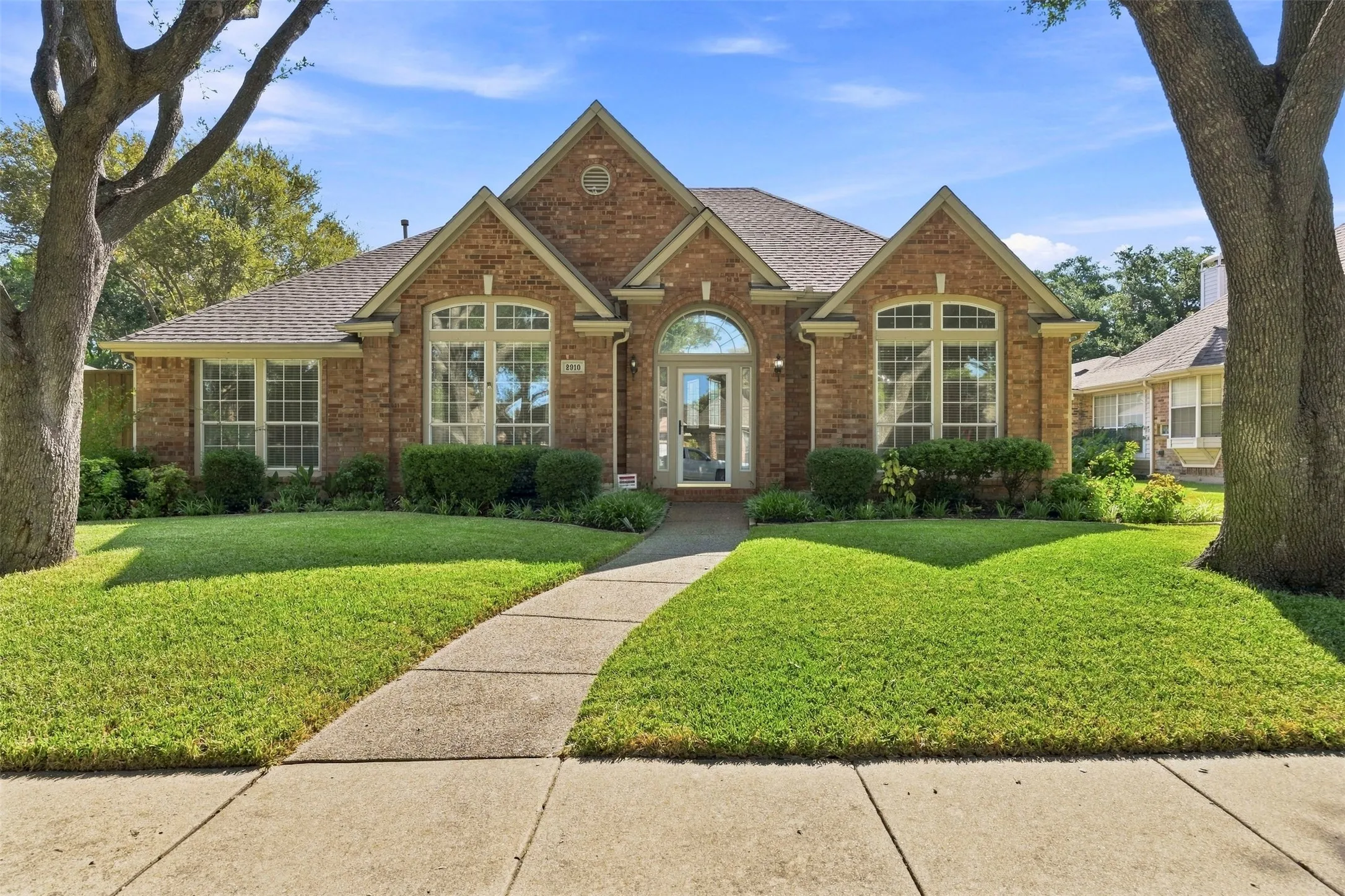 Elegant brick Colonial estate showcasing arched entryways, multi-pane windows with decorative pediments, and a welcoming covered entry portico