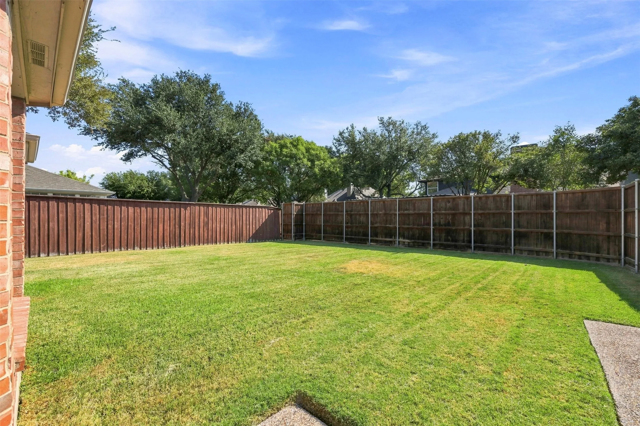 Expansive backyard featuring a manicured lawn, wood privacy fencing, and a concrete patio