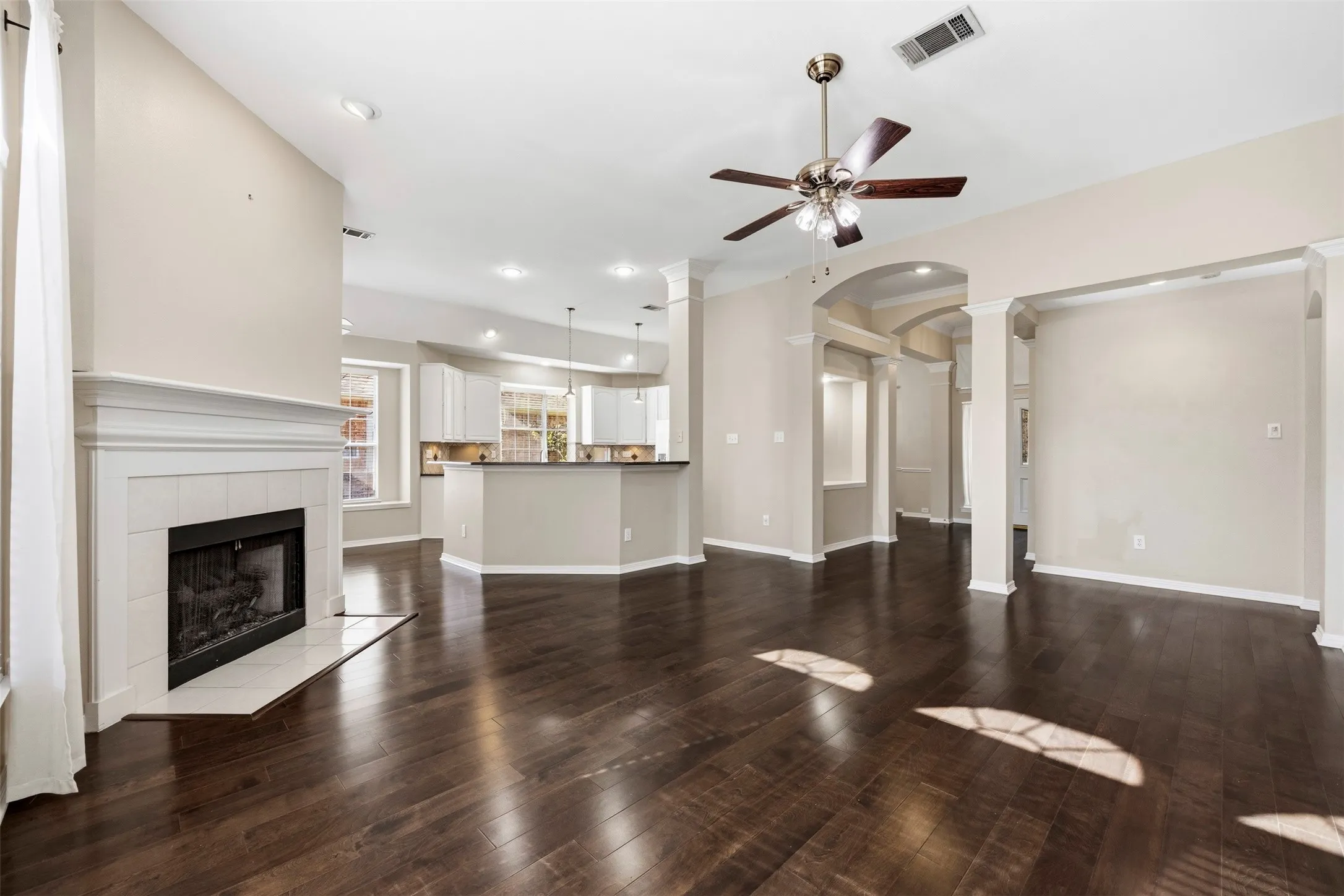 Wood-finish flooring, a white mantel fireplace, and ceiling fan with integrated lighting
