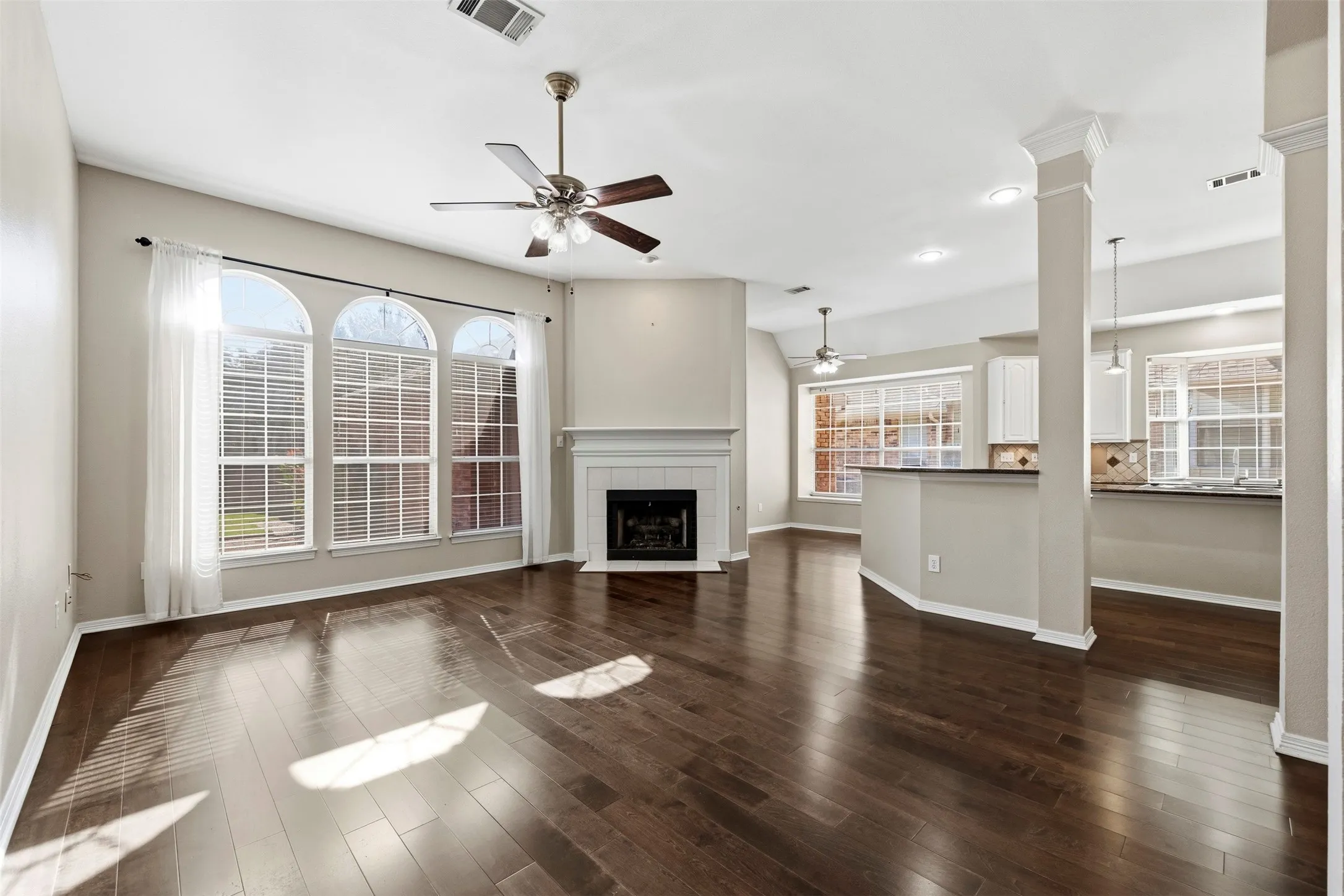 Spacious living area featuring wood-finish flooring, a fireplace with a white mantel, and arched windows