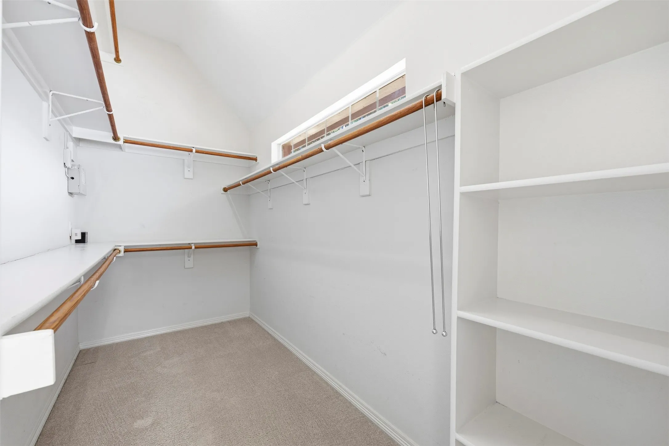 Expansive closet featuring integrated shelving, multiple wood-finish hanging rods, and a high window for natural light