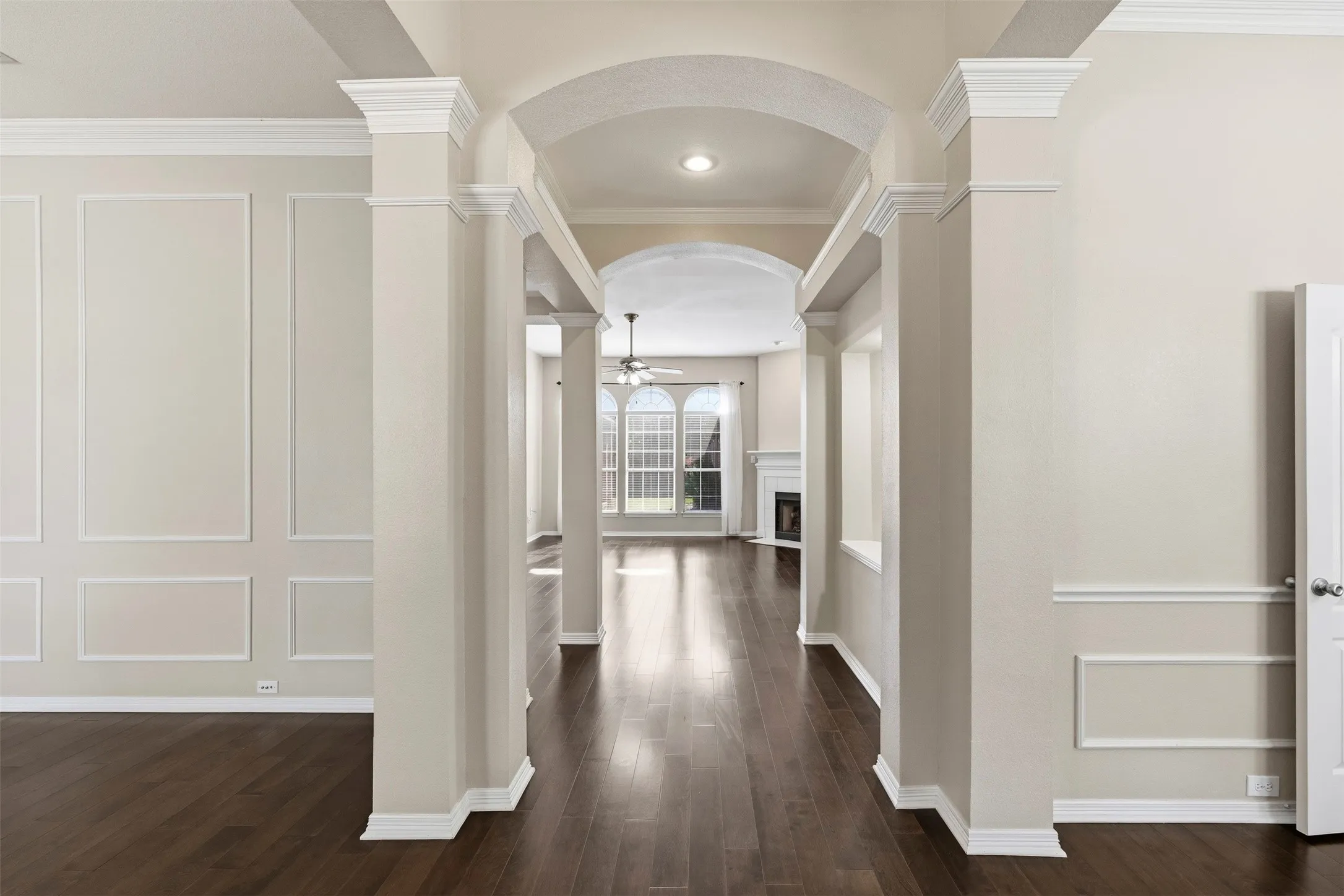 Arched entryway with substantial columns, dark wood-finish flooring, and decorative wall paneling