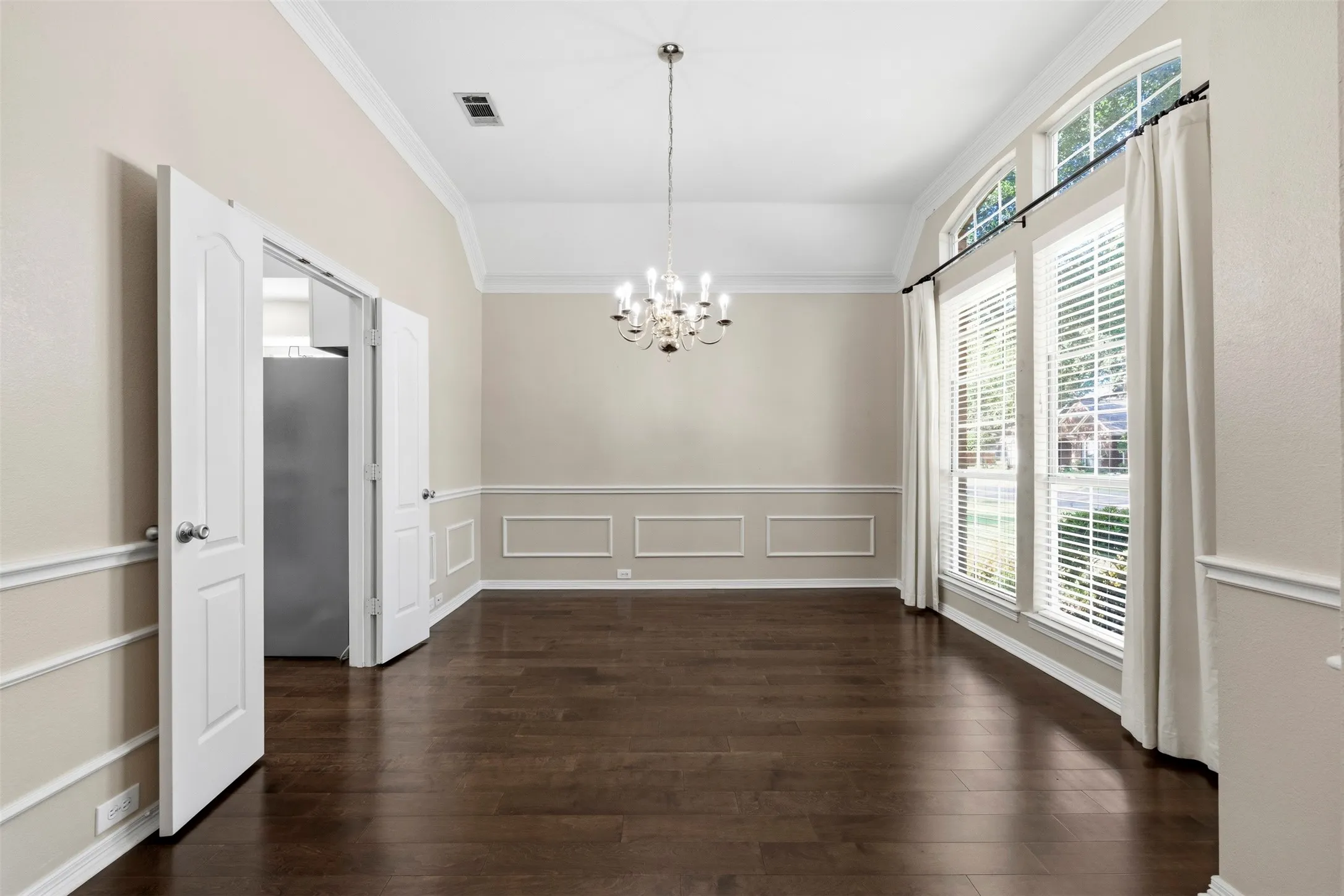 Vaulted ceiling, dark wood-finish flooring, decorative wall molding, arched transom windows, and a multi-arm chandelier