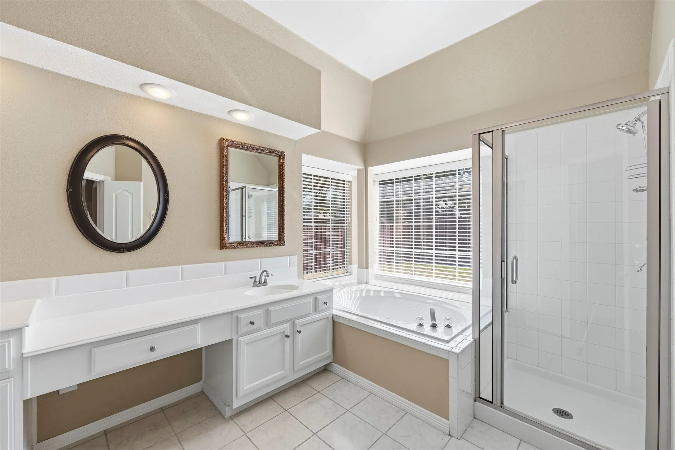 White vanity with integrated sink, expansive countertop, white tile flooring, built-in corner bathtub, and a glass-enclosed shower