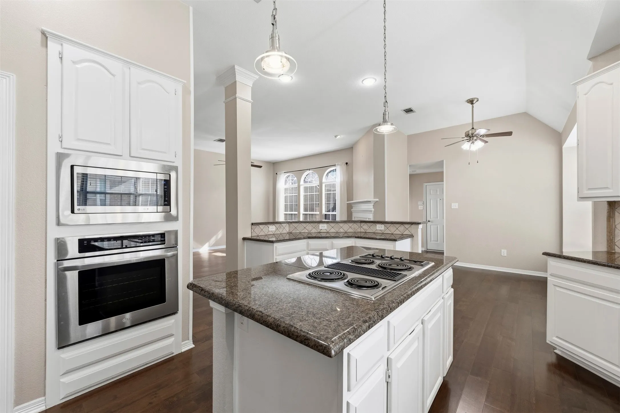 Kitchen featuring an island with a built-in cooktop, white cabinetry, granite countertops, and stainless steel built-in appliances