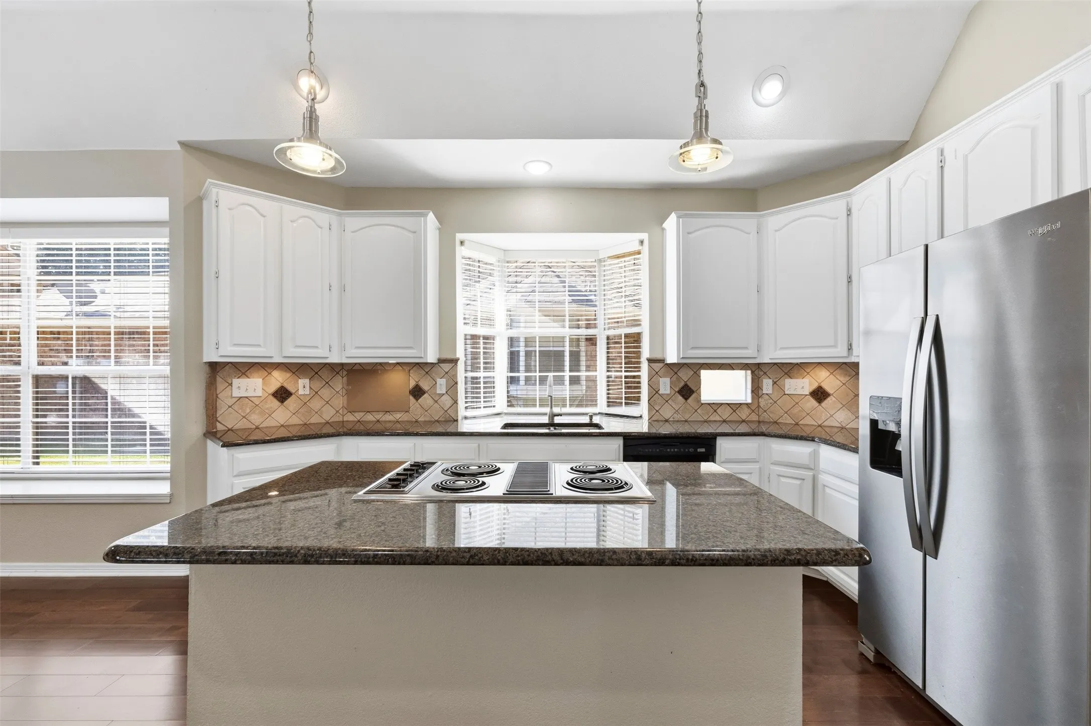 Kitchen featuring a center island cooktop, white cabinetry, stainless steel appliances, a bay window, and pendant lighting