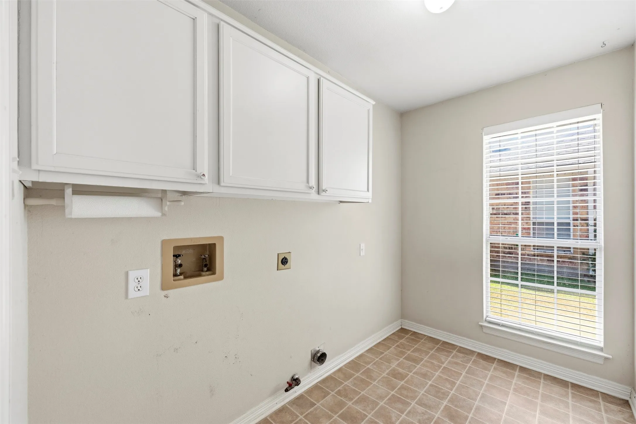 Upper cabinetry, tiled flooring, window with blinds, and white baseboards