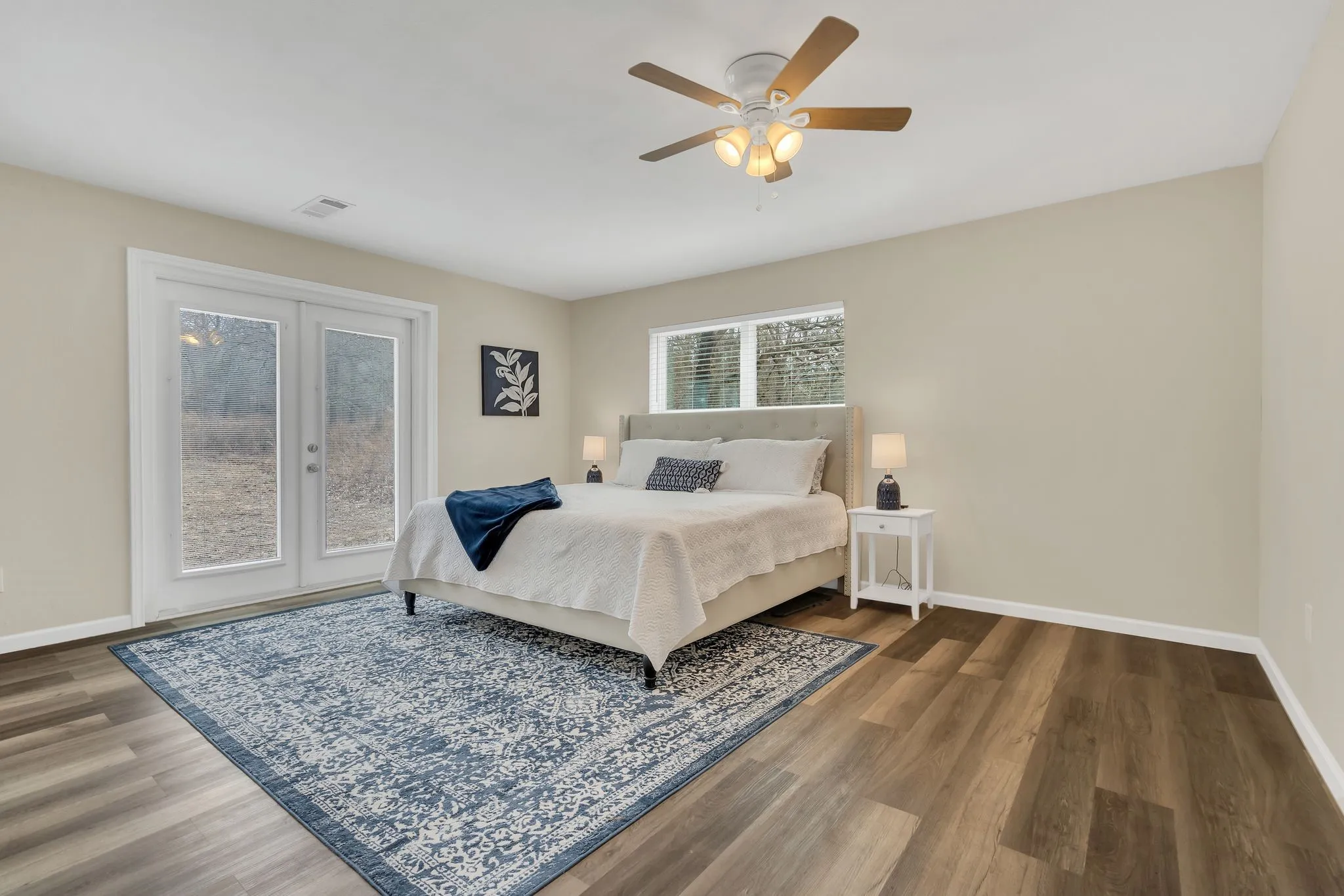 Wood-finish flooring, light-toned walls, ceiling fan with integrated lighting, glass-paneled double doors, and a single window with blinds