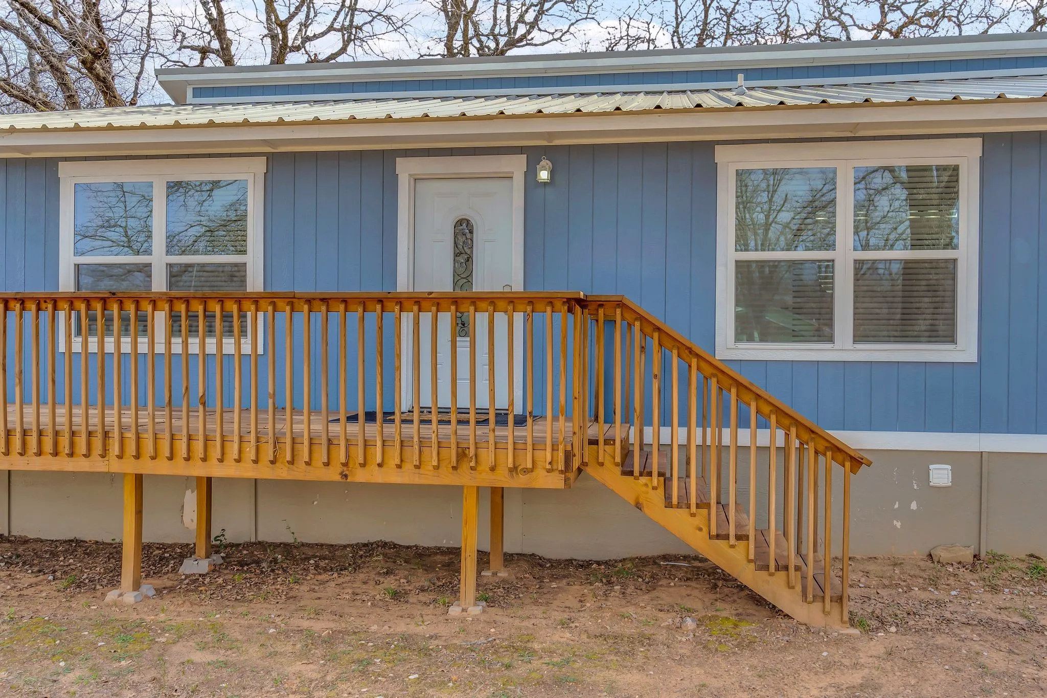 Light blue vertical siding exterior with white trim, wood front porch and railings, white entry door with decorative glass, and a metal roof