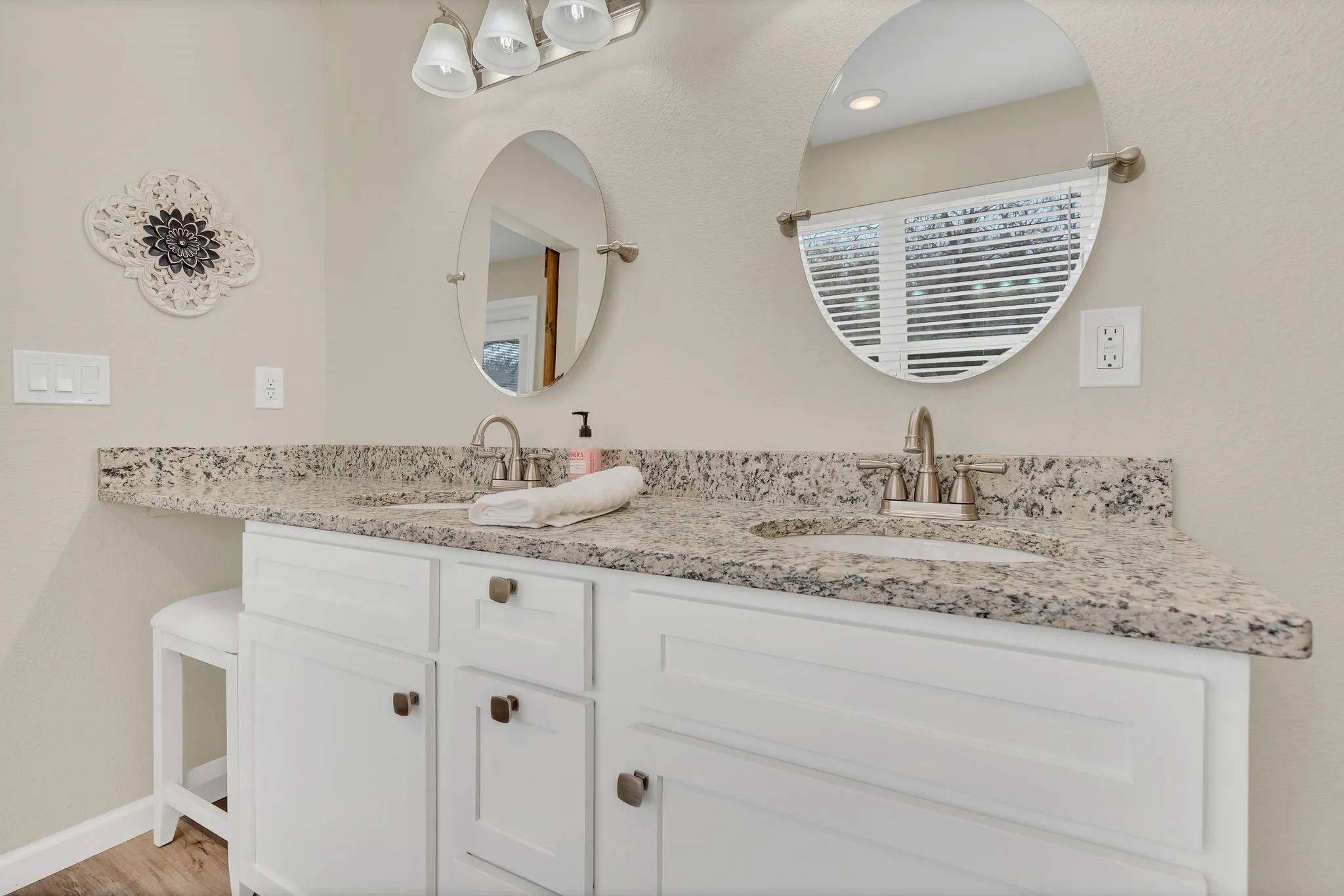 Double vanity with white cabinetry, integrated sinks, granite countertop, and dual circular mirrors