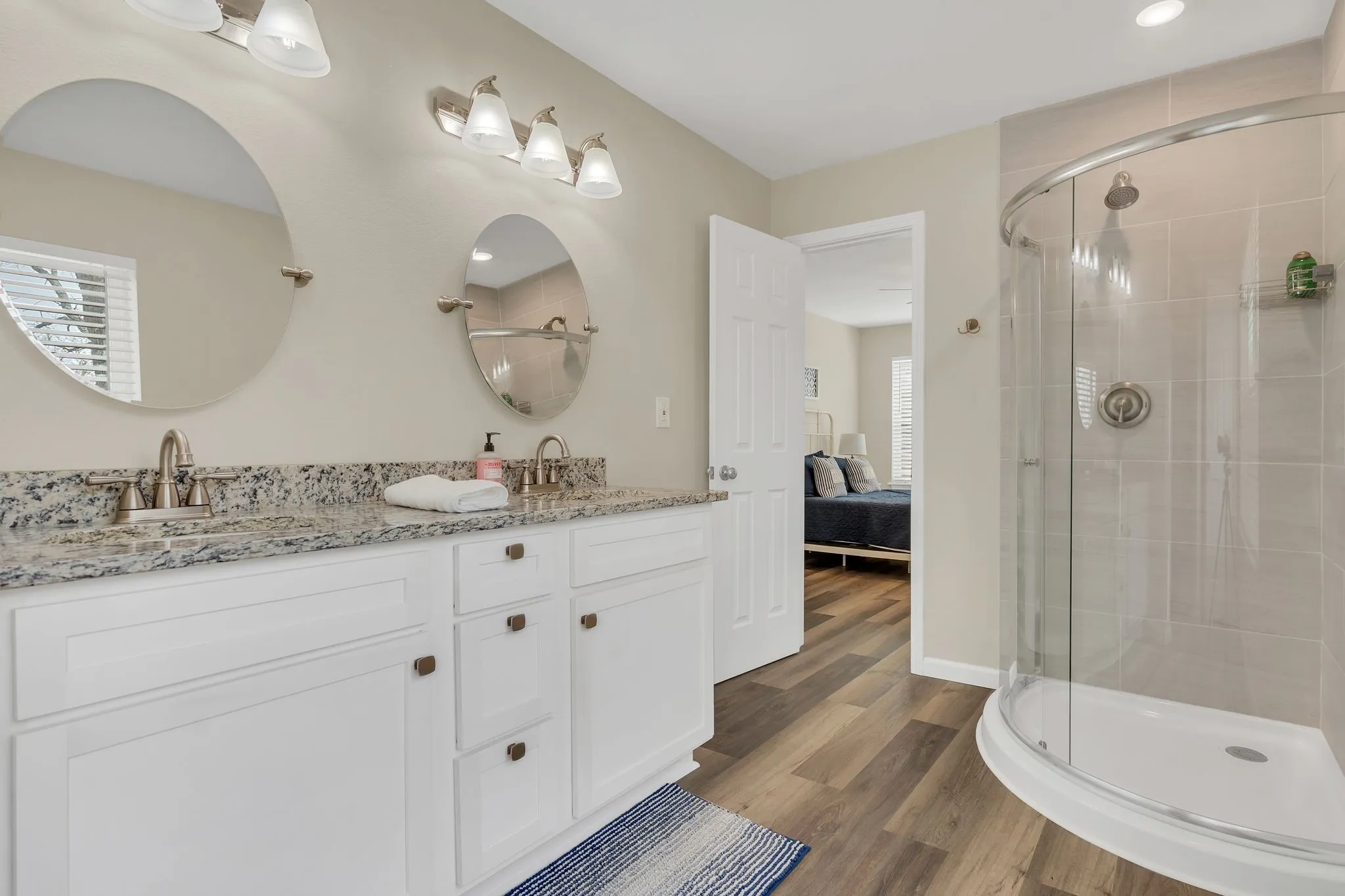 Dual sink vanity with granite-style countertop, white cabinetry, and wood-finish flooring