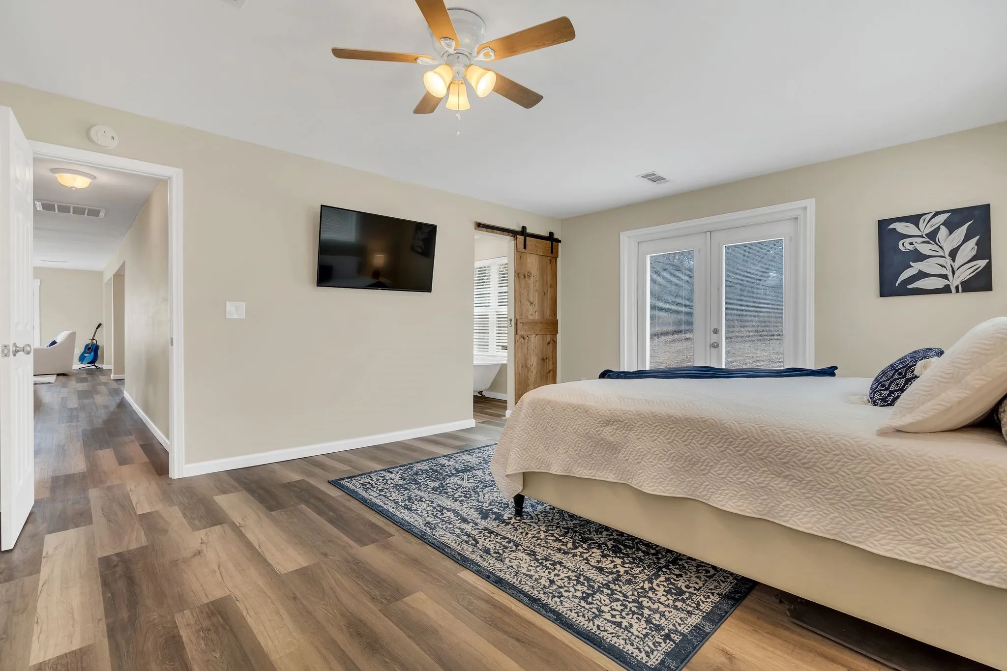 Wood-finish flooring throughout, ceiling fan with integrated lighting, double French doors, and a wood barn door