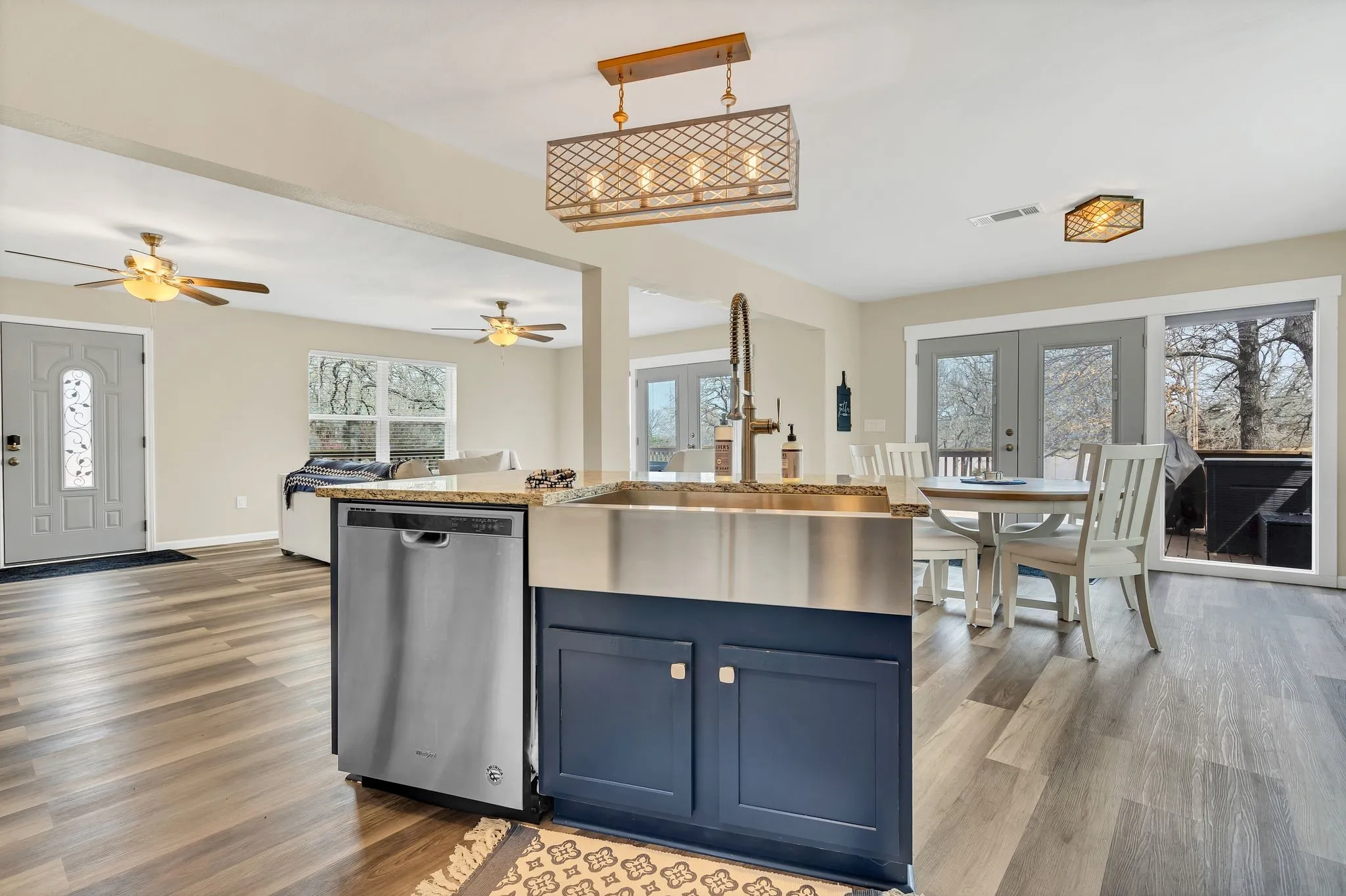 Open-concept living space featuring wood-finish flooring, a kitchen island with a farmhouse sink, stainless steel appliances, and French doors leading to an outdoor deck