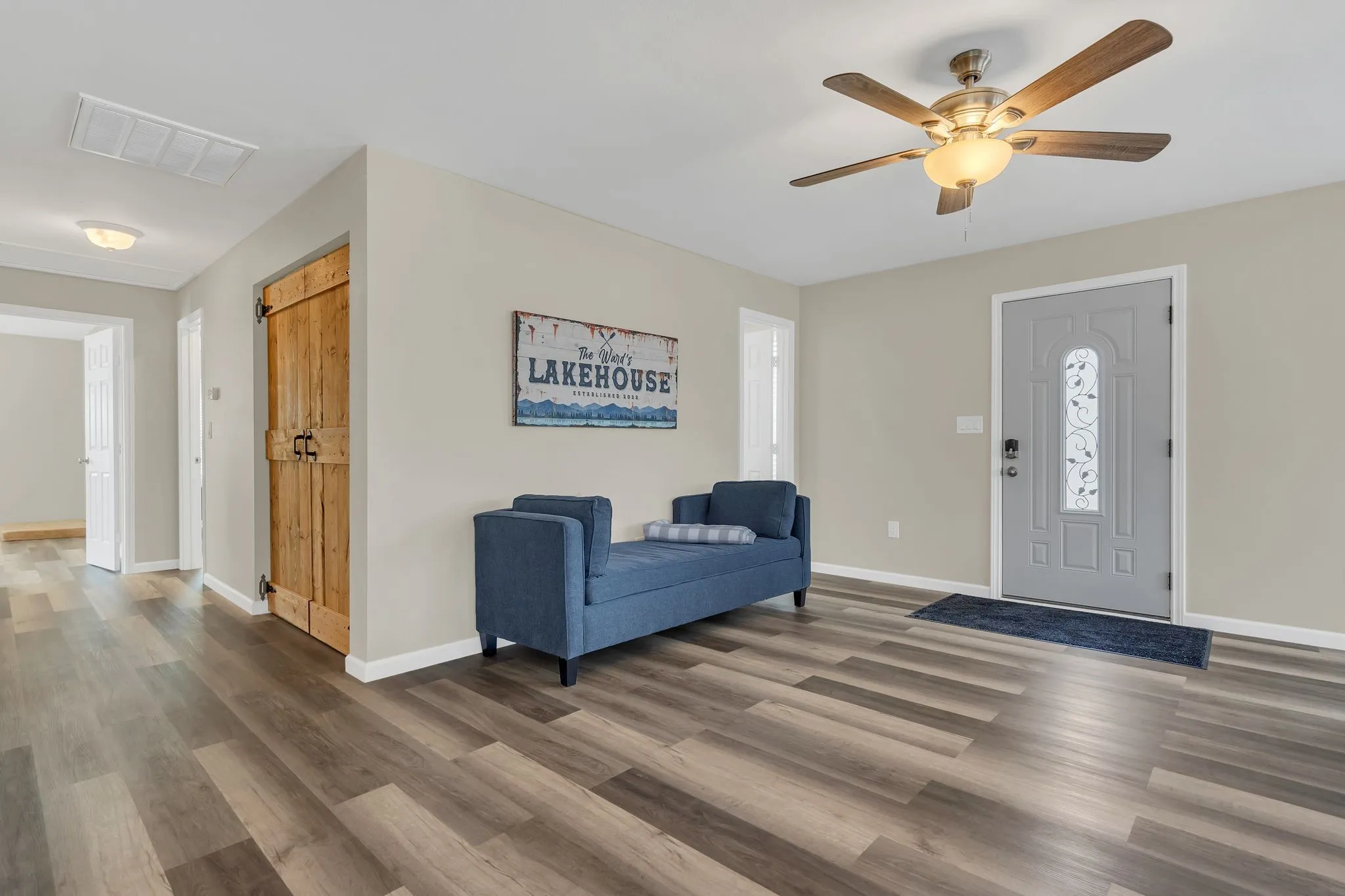 Wood-finish flooring, ceiling fan with integrated lighting, paneled entry door with decorative glass inlay, and a rustic wood barn door