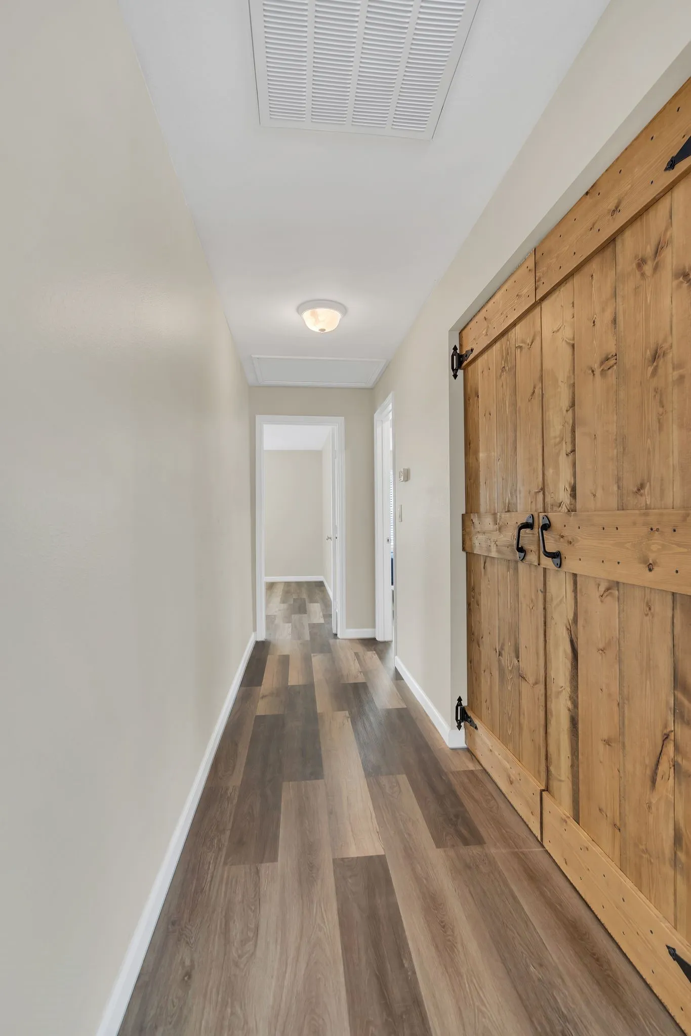 Wood-finish flooring throughout, barn-style doors with black hardware, and overhead flush-mount lighting