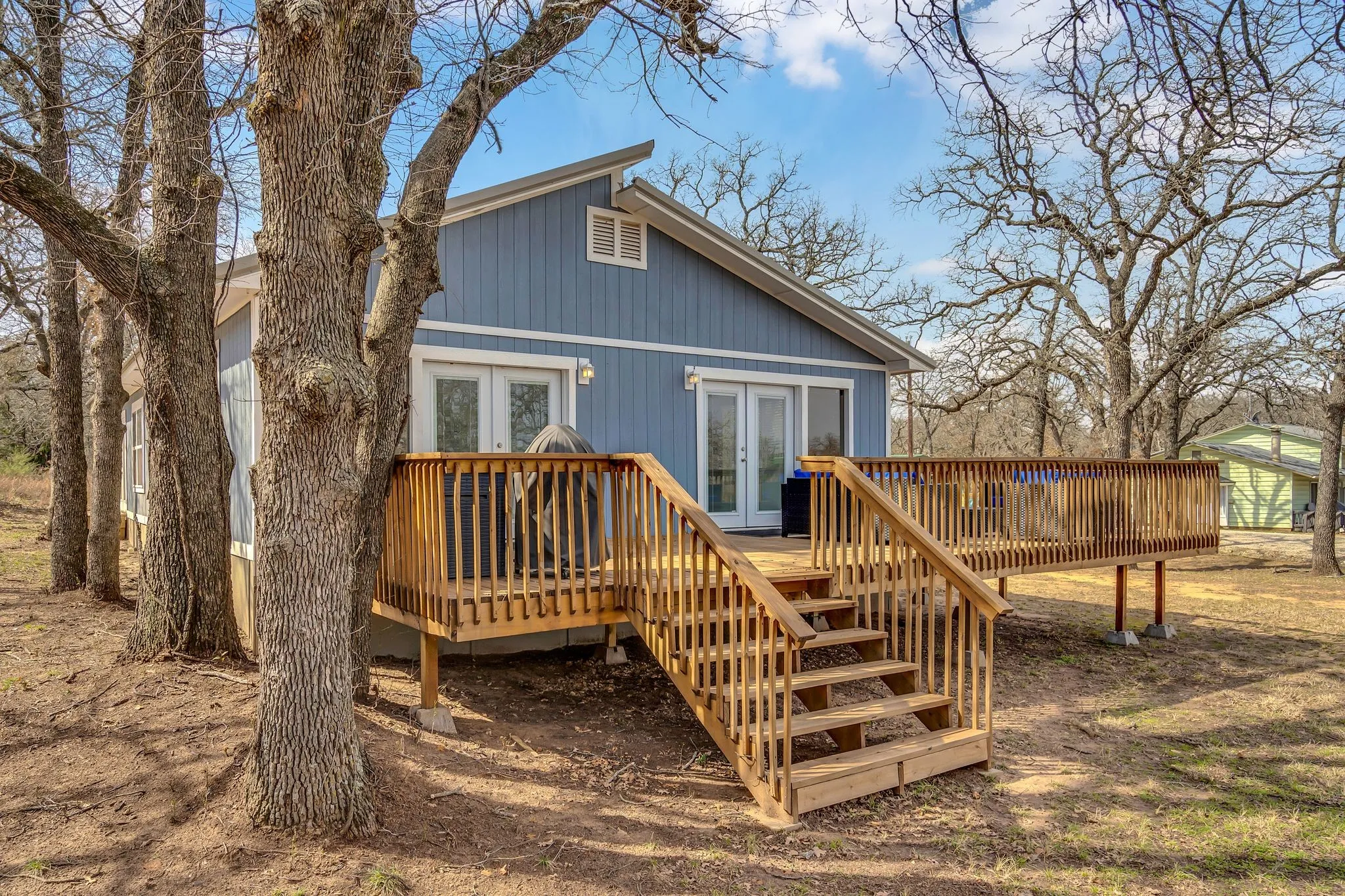 Exterior featuring a natural wood deck with railings, blue siding, a white gable vent, and double French doors
