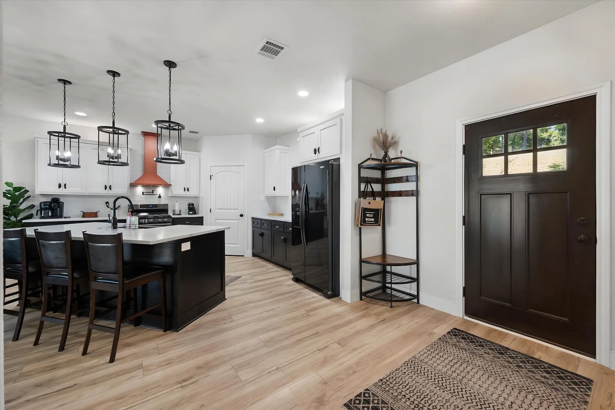 Welcoming entry flows into the spacious kitchen with statement lighting, oversized island, modern finishes, and warm luxury vinyl plank flooring.