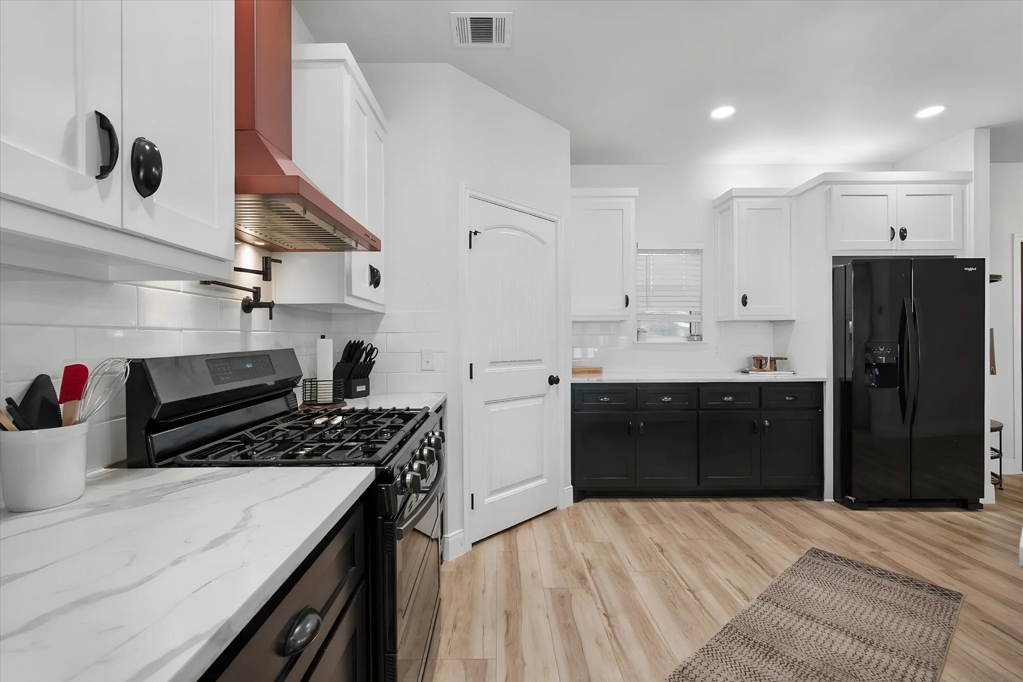 Well-equipped kitchen features a gas range, striking copper vent hood, plentiful cabinetry, pantry storage, and stylish contrasting finishes.