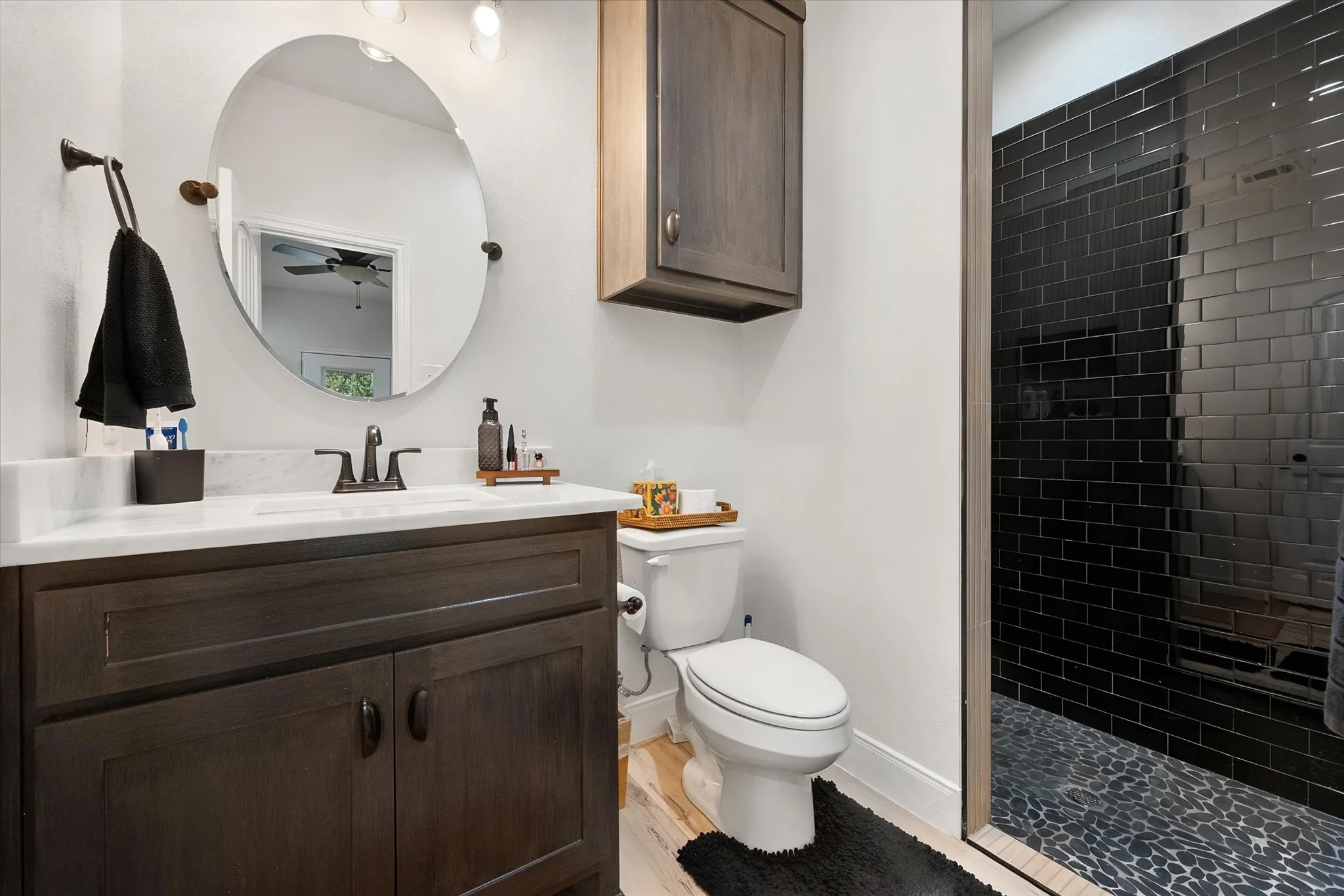 Stylish bathroom features a dark tiled shower, modern vanity, round mirror, contemporary fixtures, and sophisticated contrasting finishes.