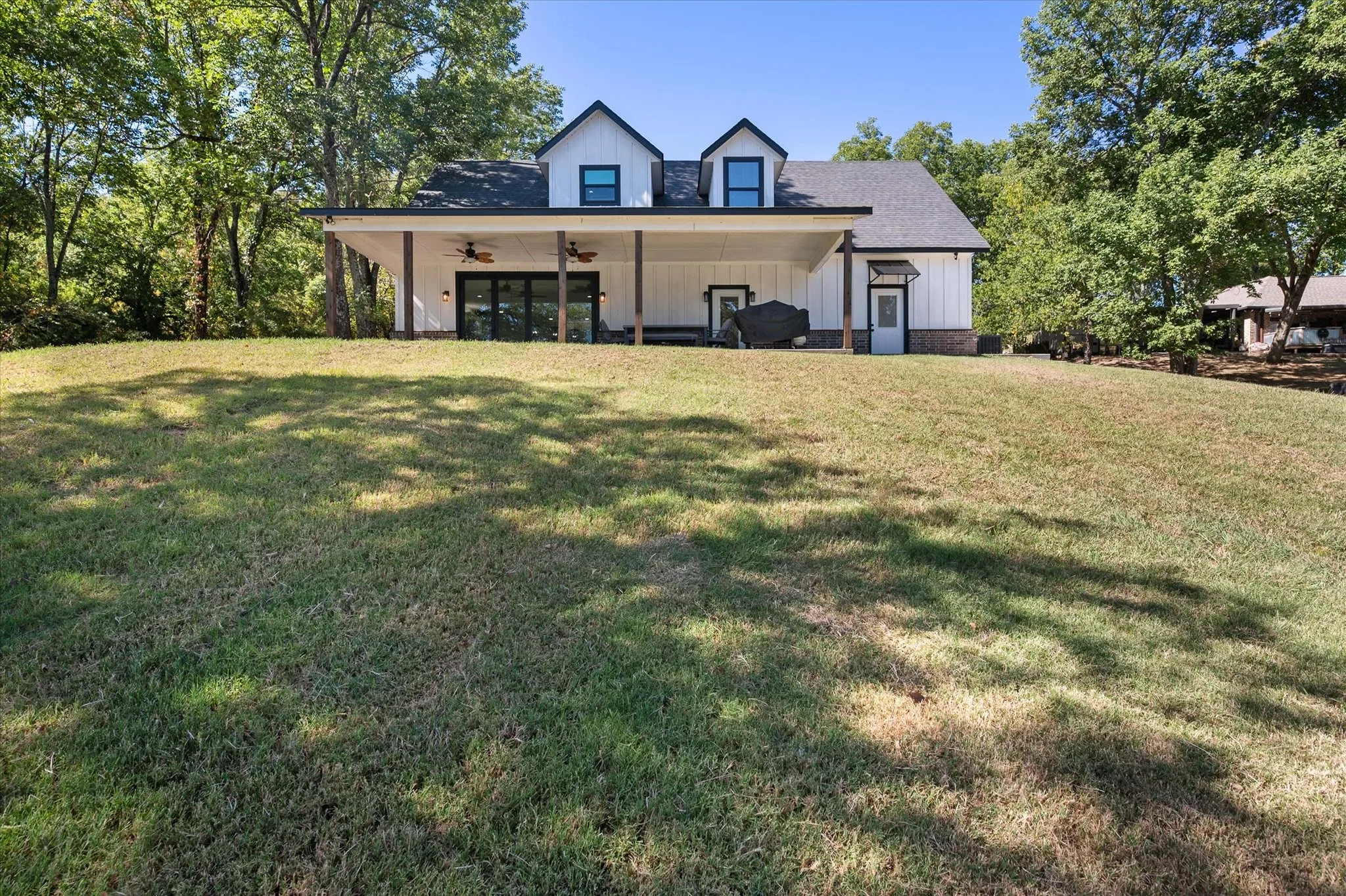 Large gently sloping backyard provides an open lawn beneath mature trees with the modern farmhouse positioned above the Richland Chambers Lake shoreline.