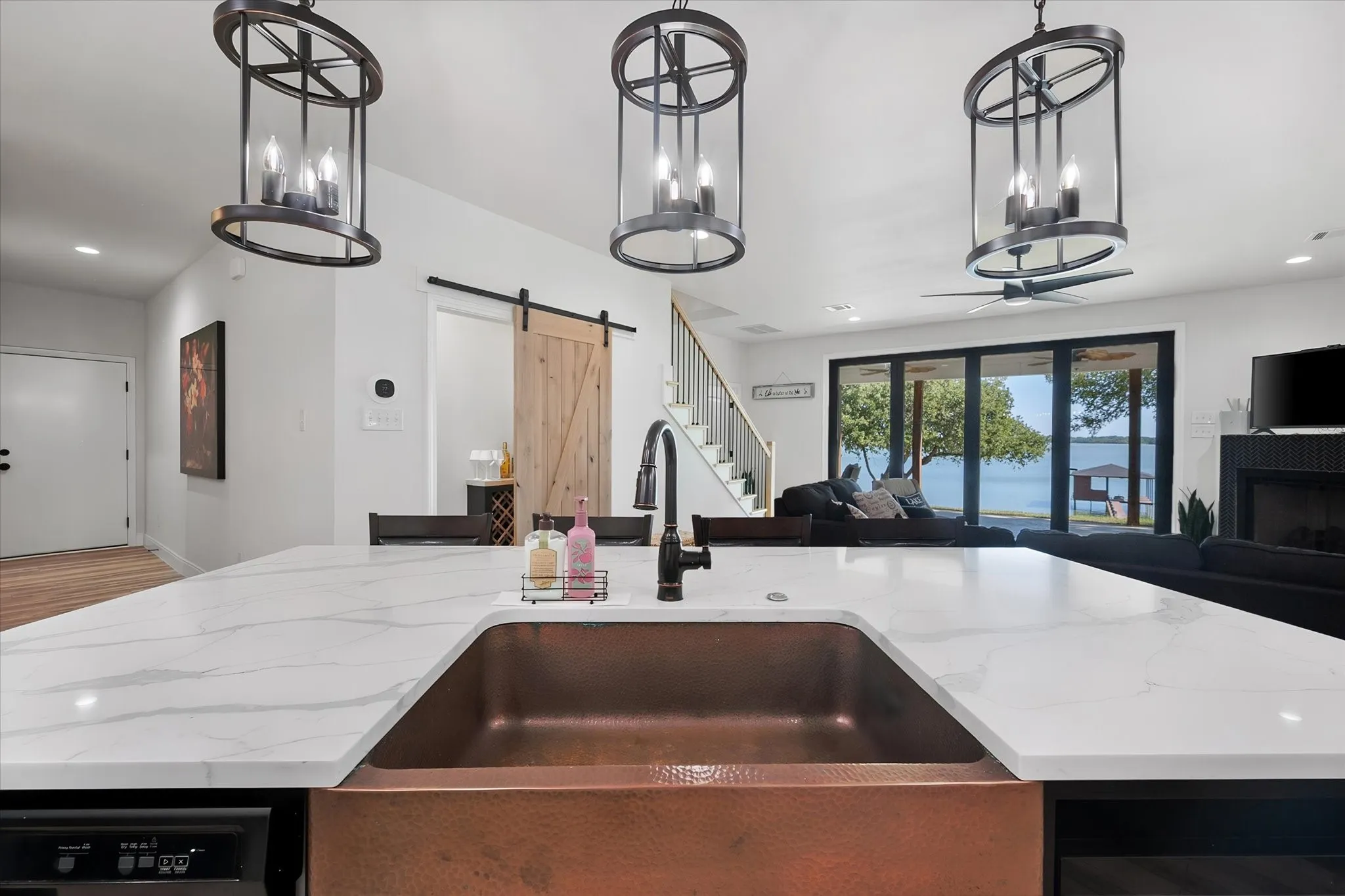 Distinctive copper farmhouse sink anchors the oversized kitchen island with beautiful lake views visible beyond the open living area.