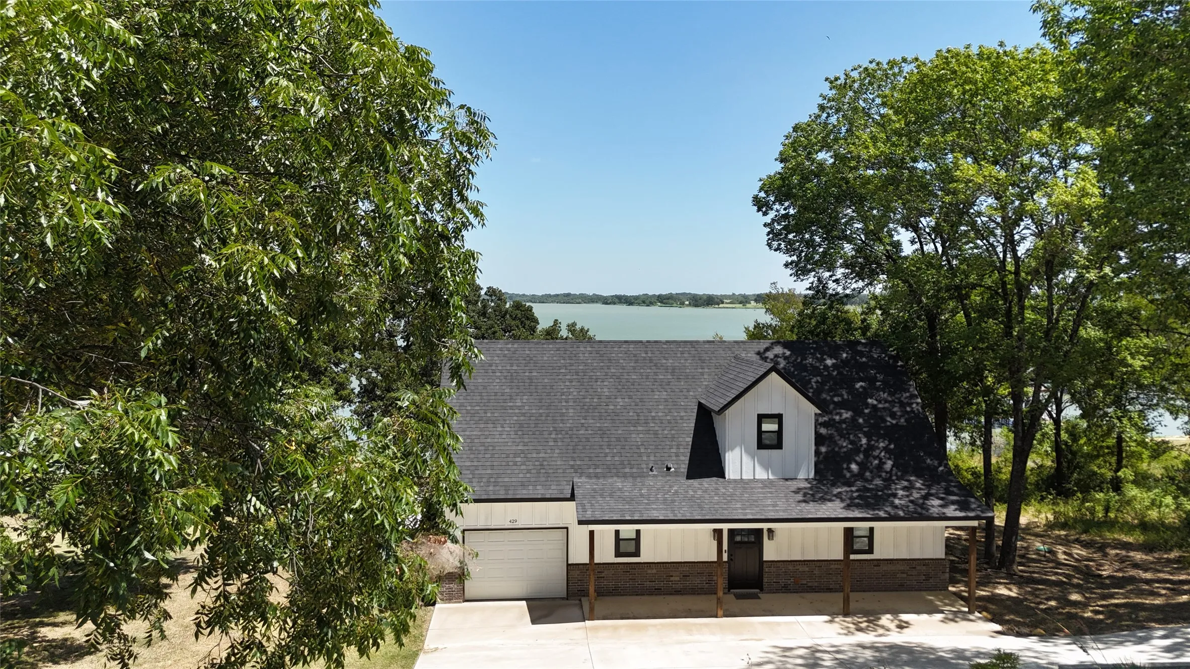 Aerial perspective captures the lake house tucked among mature trees with Richland Chambers Lake creating a spectacular backdrop beyond the home.