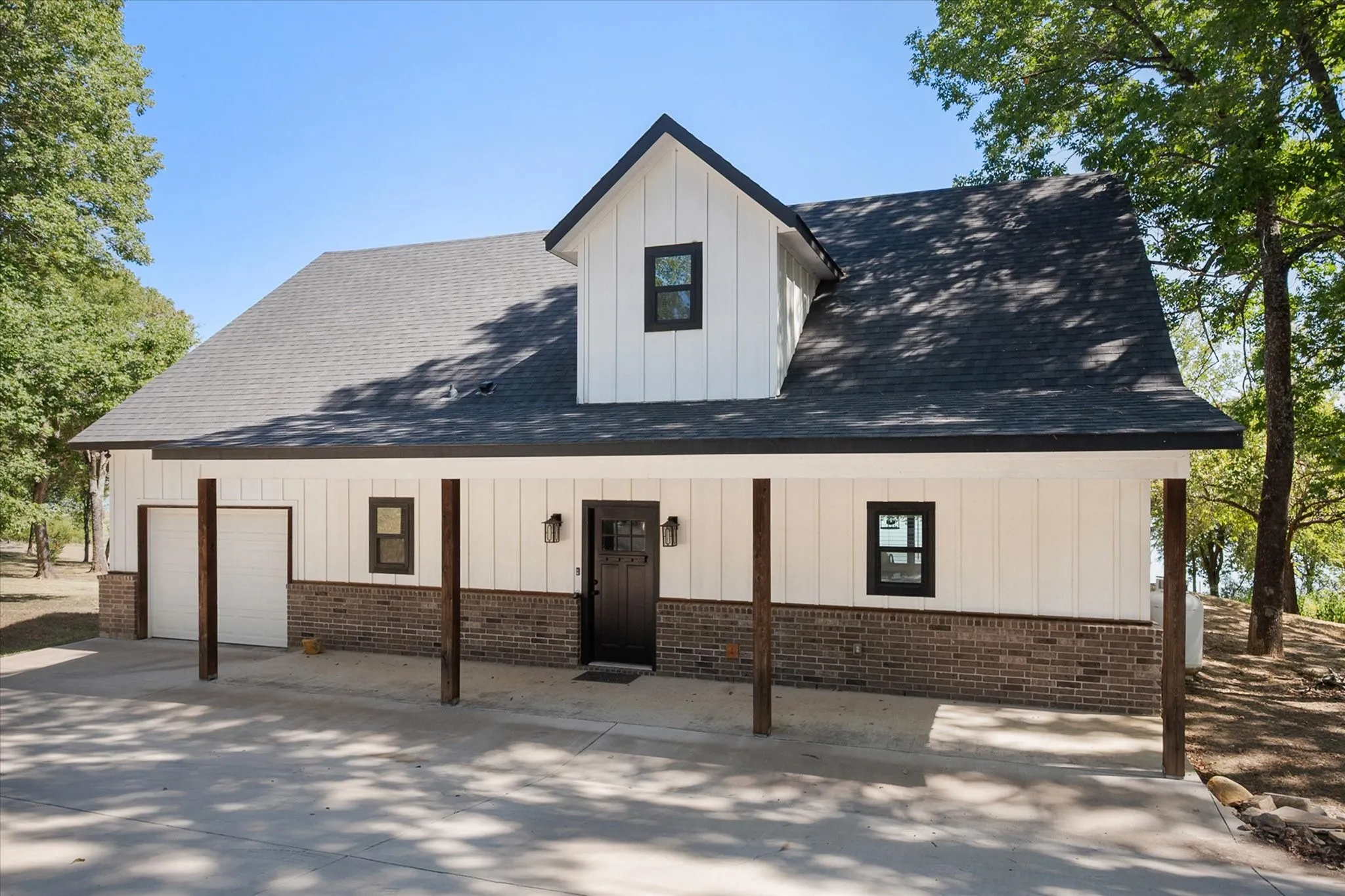 Charming modern farmhouse exterior features crisp white siding, brick accents, a covered front porch, attached garage, and mature shade trees.