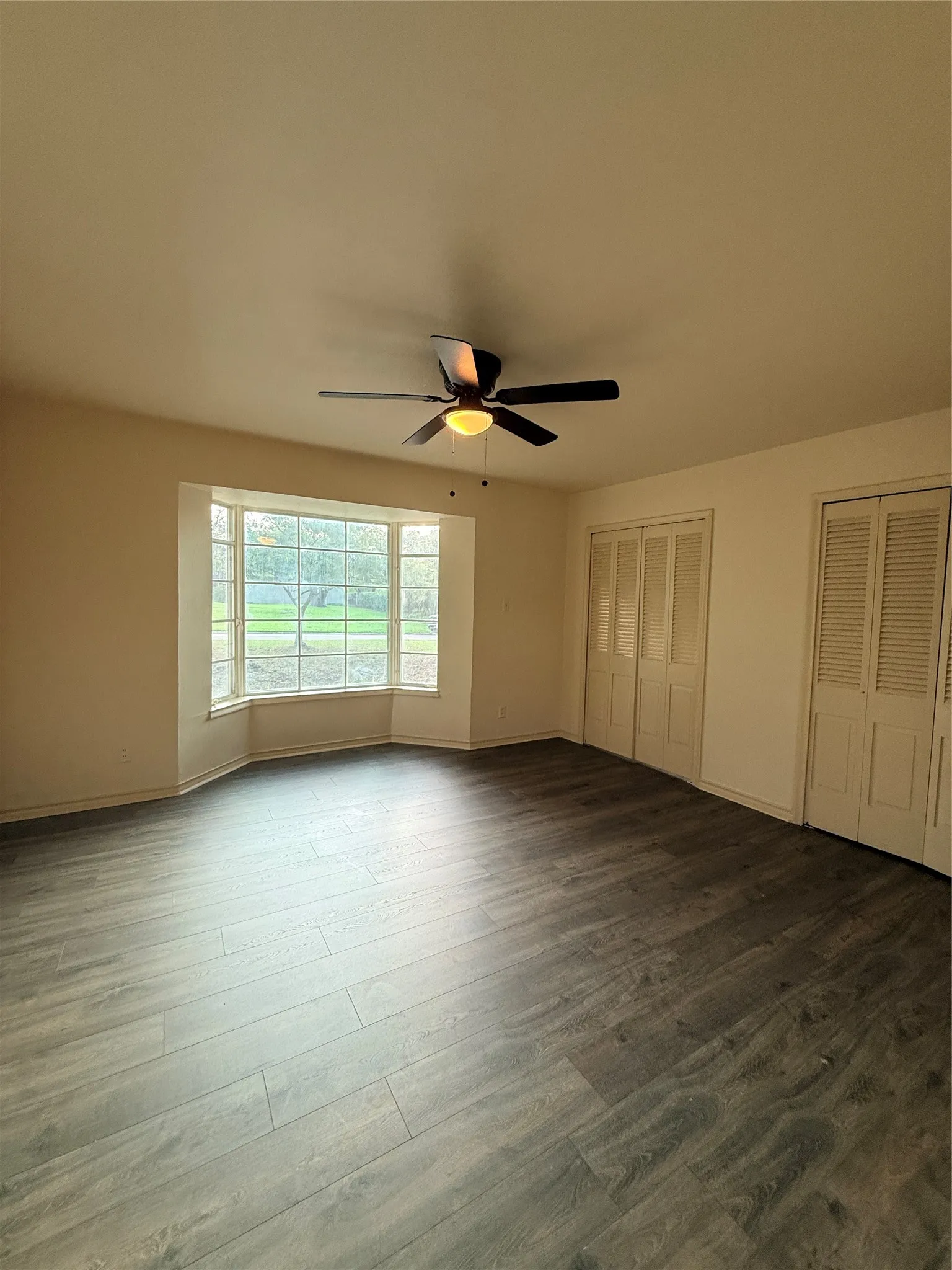 Wood-finish flooring, bay window, ceiling fan, and louvered bifold doors