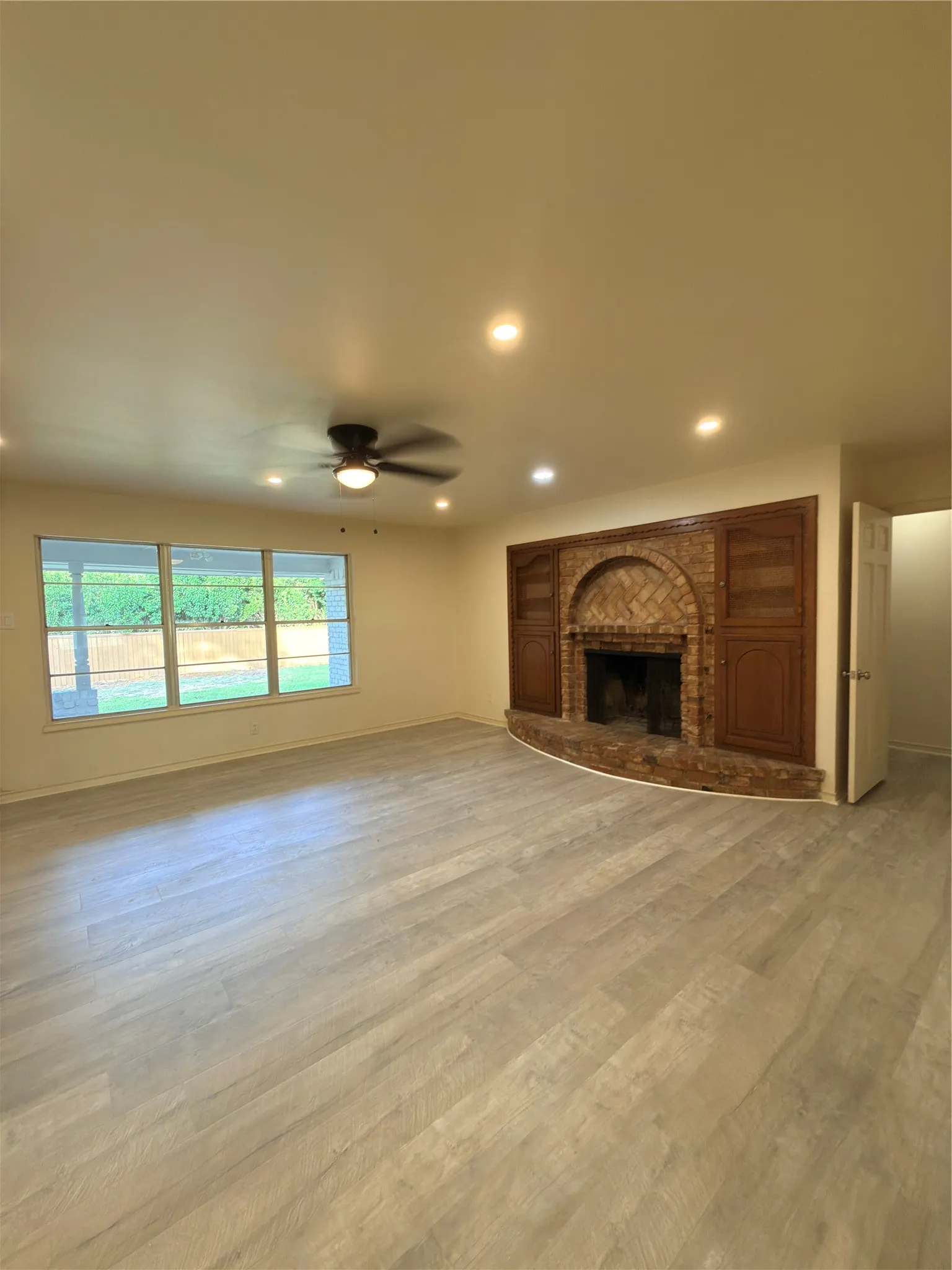 Spacious room featuring wood-finish flooring, a brick fireplace, built-in cabinetry, and recessed lighting