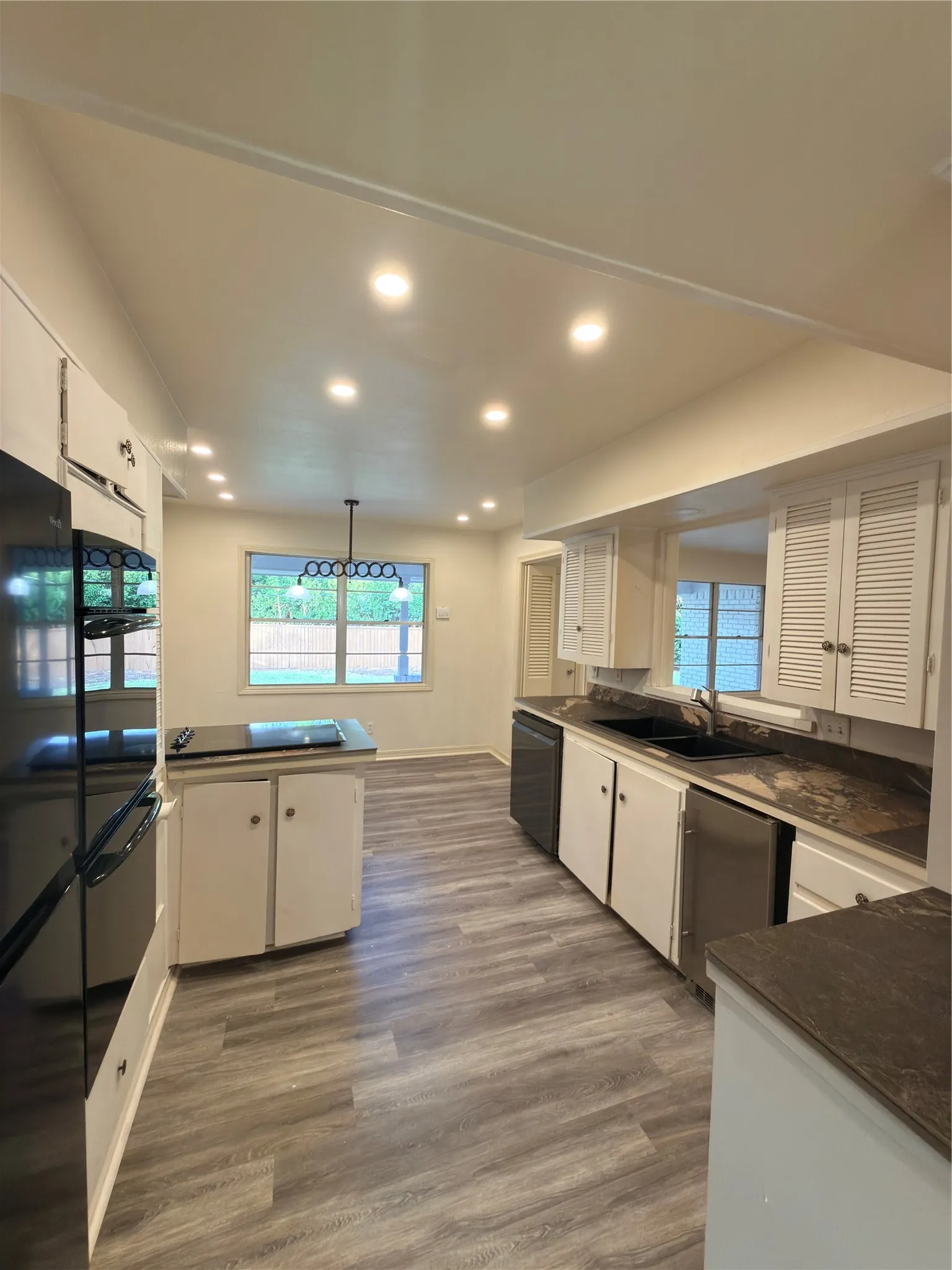 Kitchen featuring wood-finish flooring, recessed lighting, white cabinetry, dark countertops, and a black double basin sink