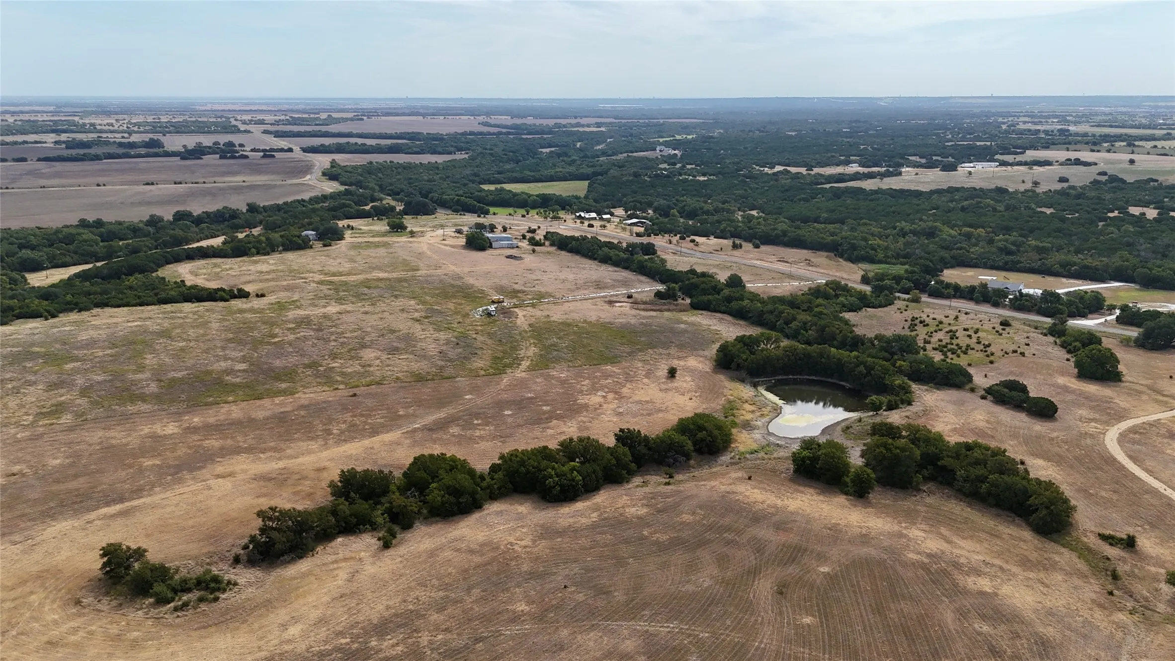 Expansive rural acreage featuring varied topography, mature trees, a natural pond, and distant structures