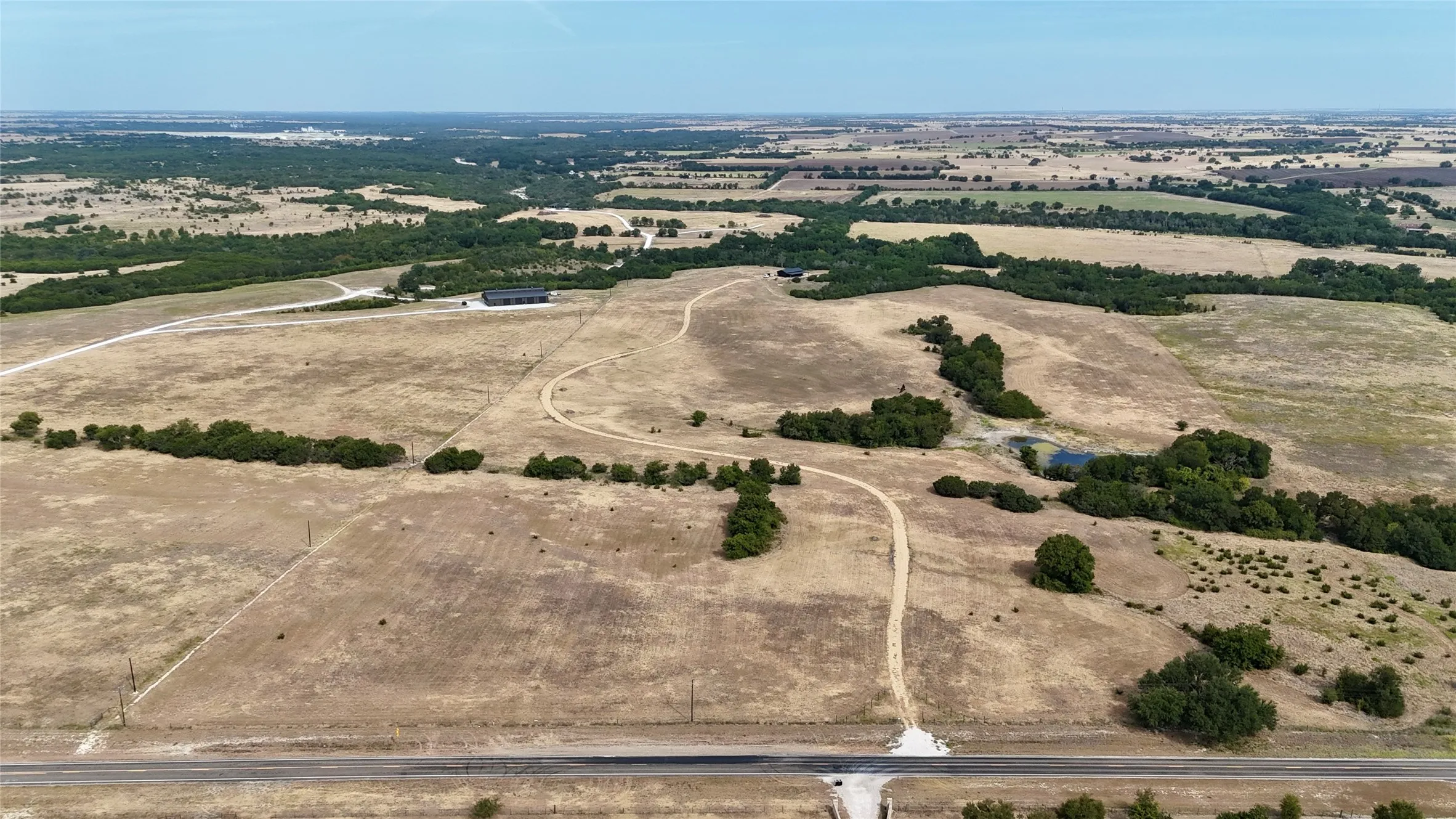 Expansive agricultural land featuring a paved road frontage, natural ponds, and scattered tree clusters